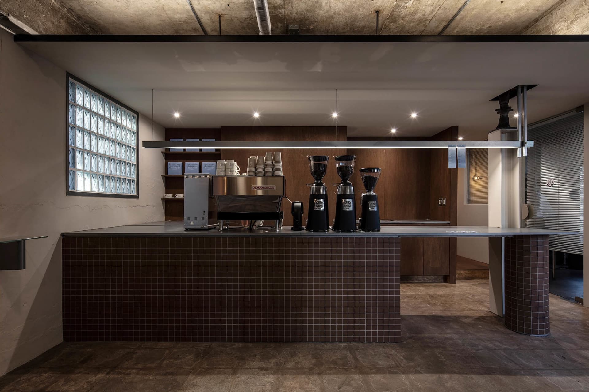 An industrial-style coffee shop counter with concrete walls and a tiled bar.