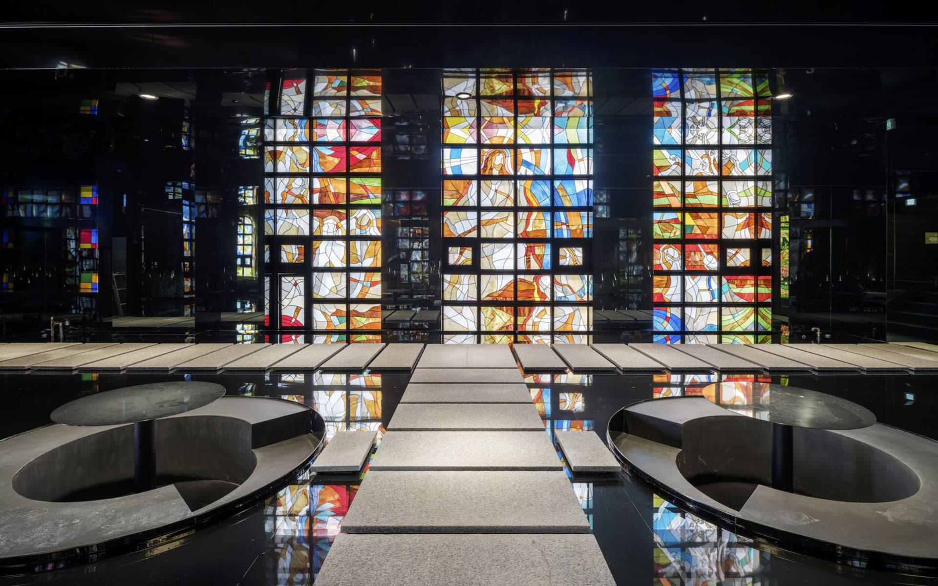 A spacious church interior with concrete flooring and vibrant stained-glass windows.