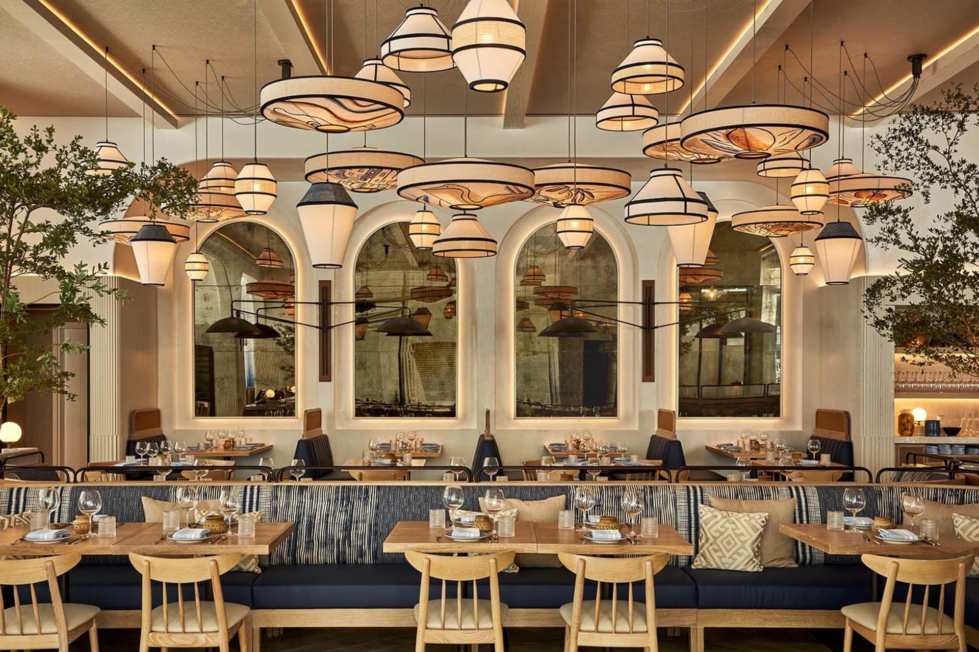 A modern restaurant interior with wooden tables, upholstered benches, and hanging pendant lights.