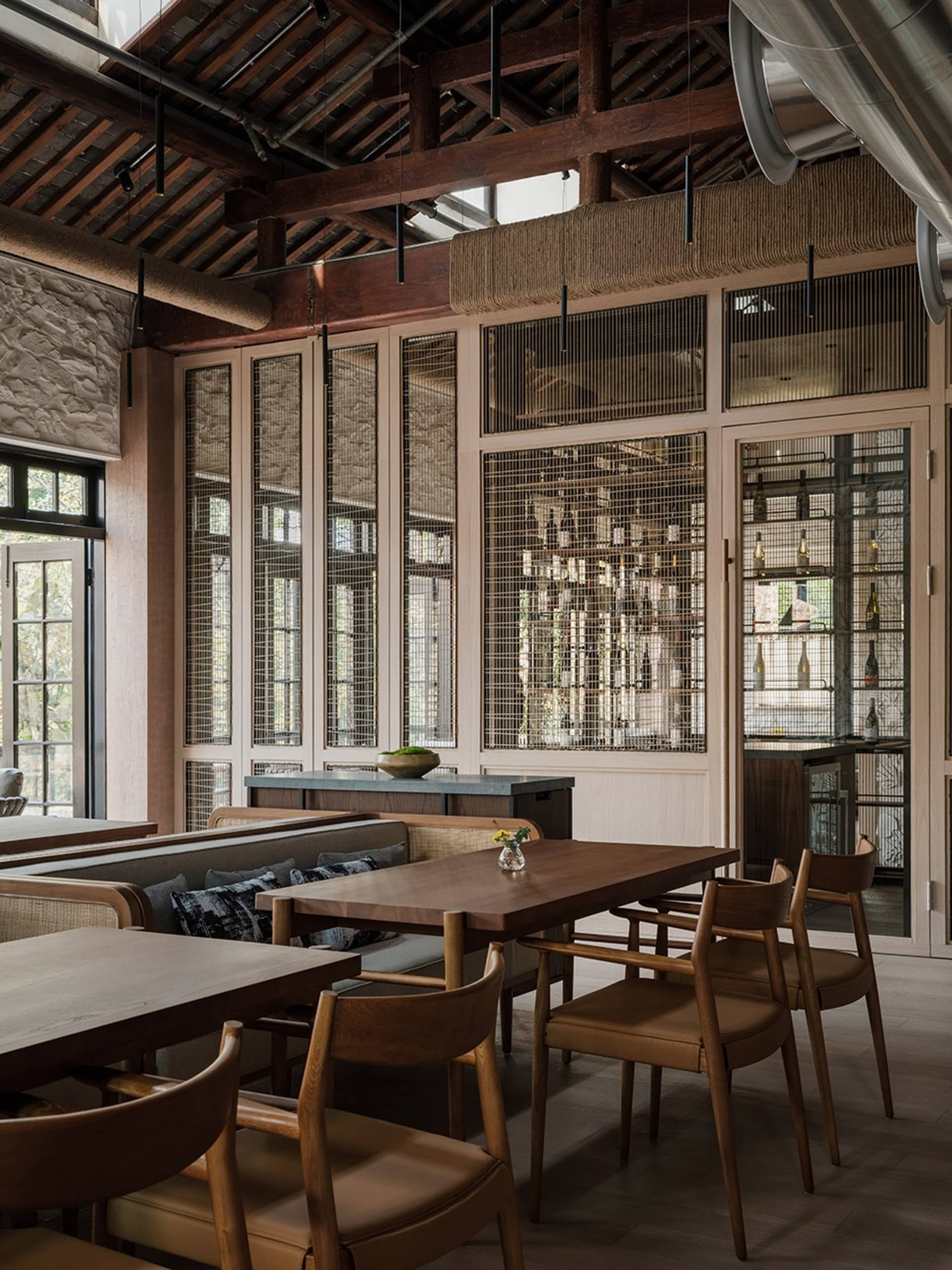 現代餐廳室內，擺放木製餐桌與餐椅，並有裸露的木樑與椽子。