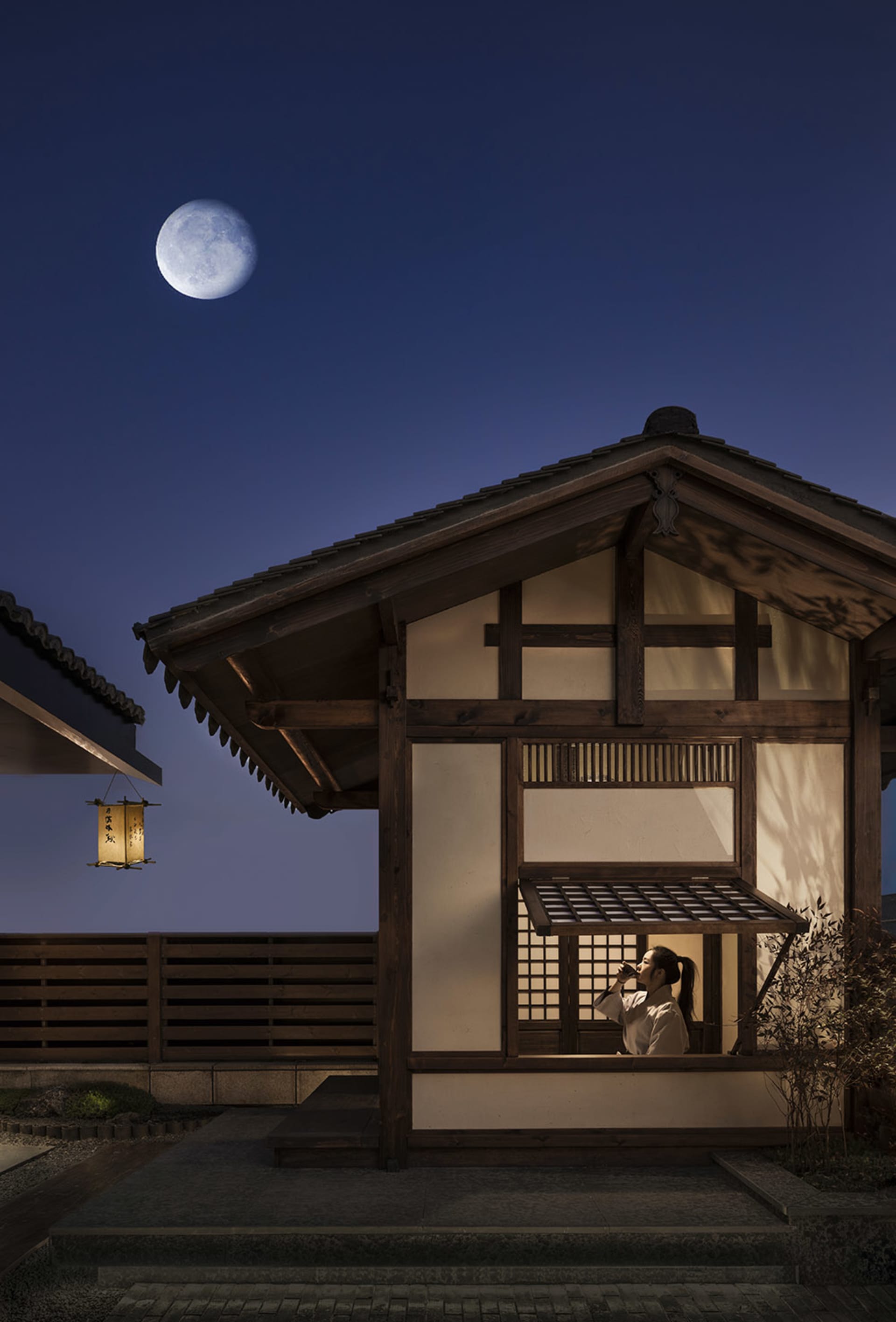 傳統日式木造建築外懸掛一盞紙燈籠,夜空清澈,月圓高懸。