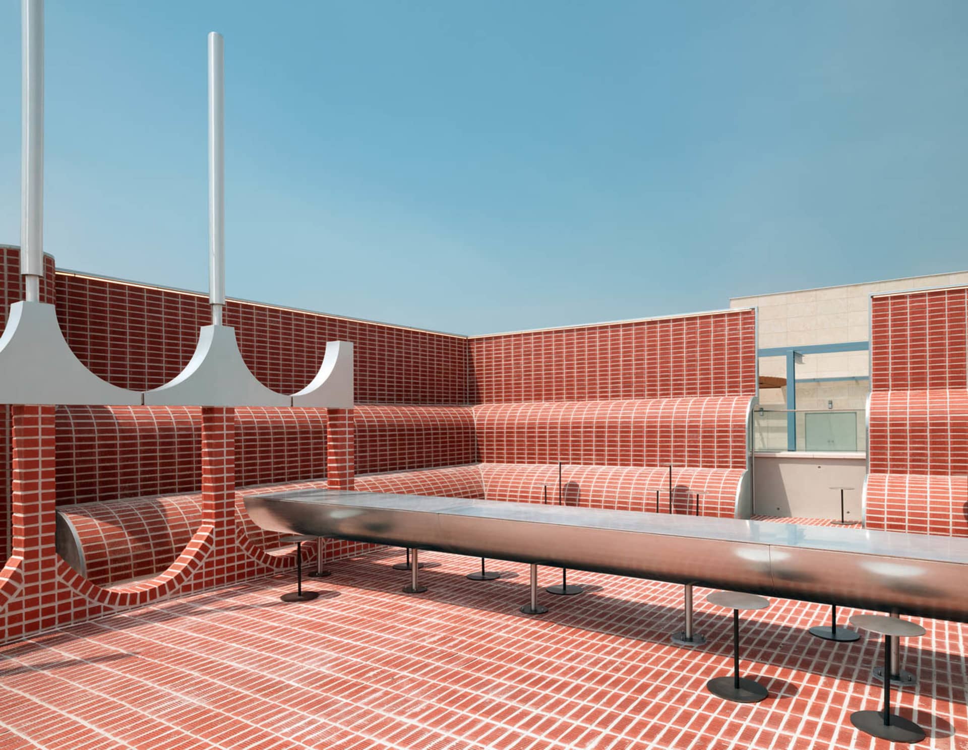 Modern, minimalist outdoor lounge area with brick walls and stainless steel benches.