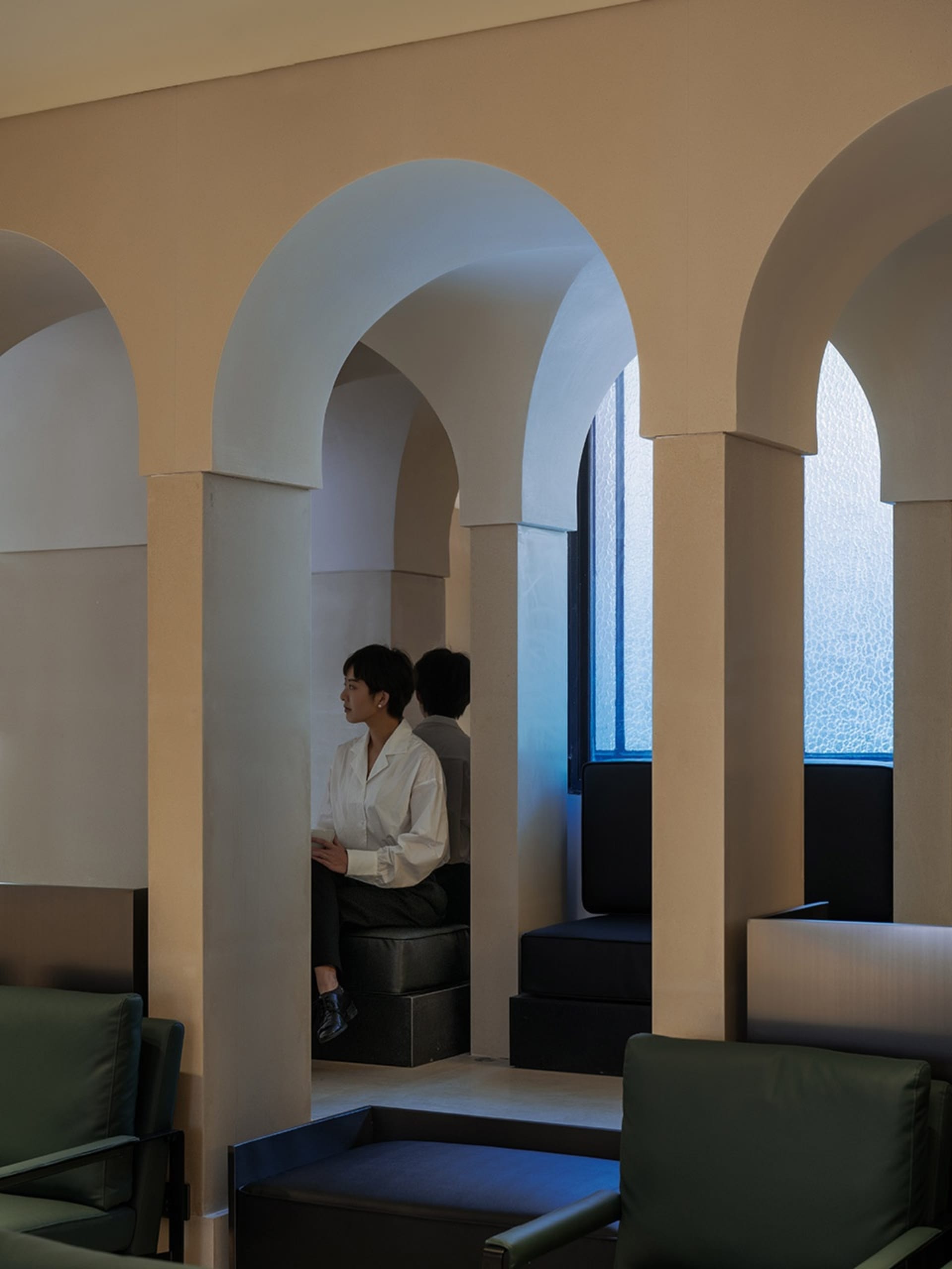 A person in a white shirt sitting in an archway within a concrete interior space.