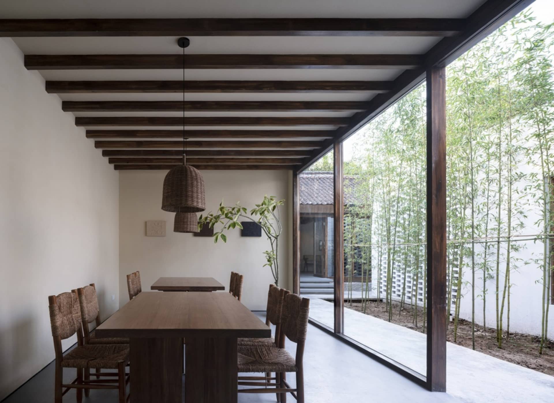 A minimalist dining room with a wooden table and chairs, featuring a wooden ceiling and floor-to-ceiling windows with bamboo