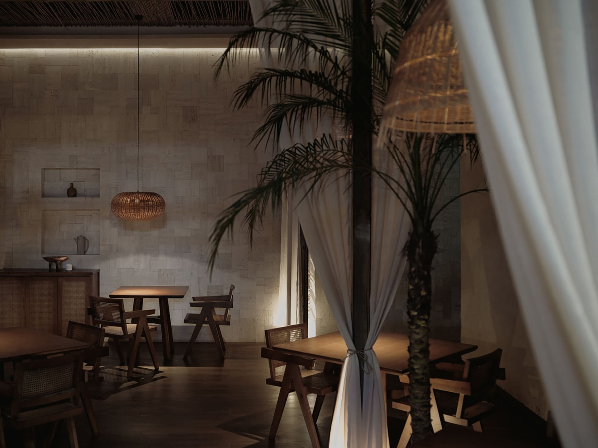 An industrial-styled restaurant interior with wooden furniture and palm trees.