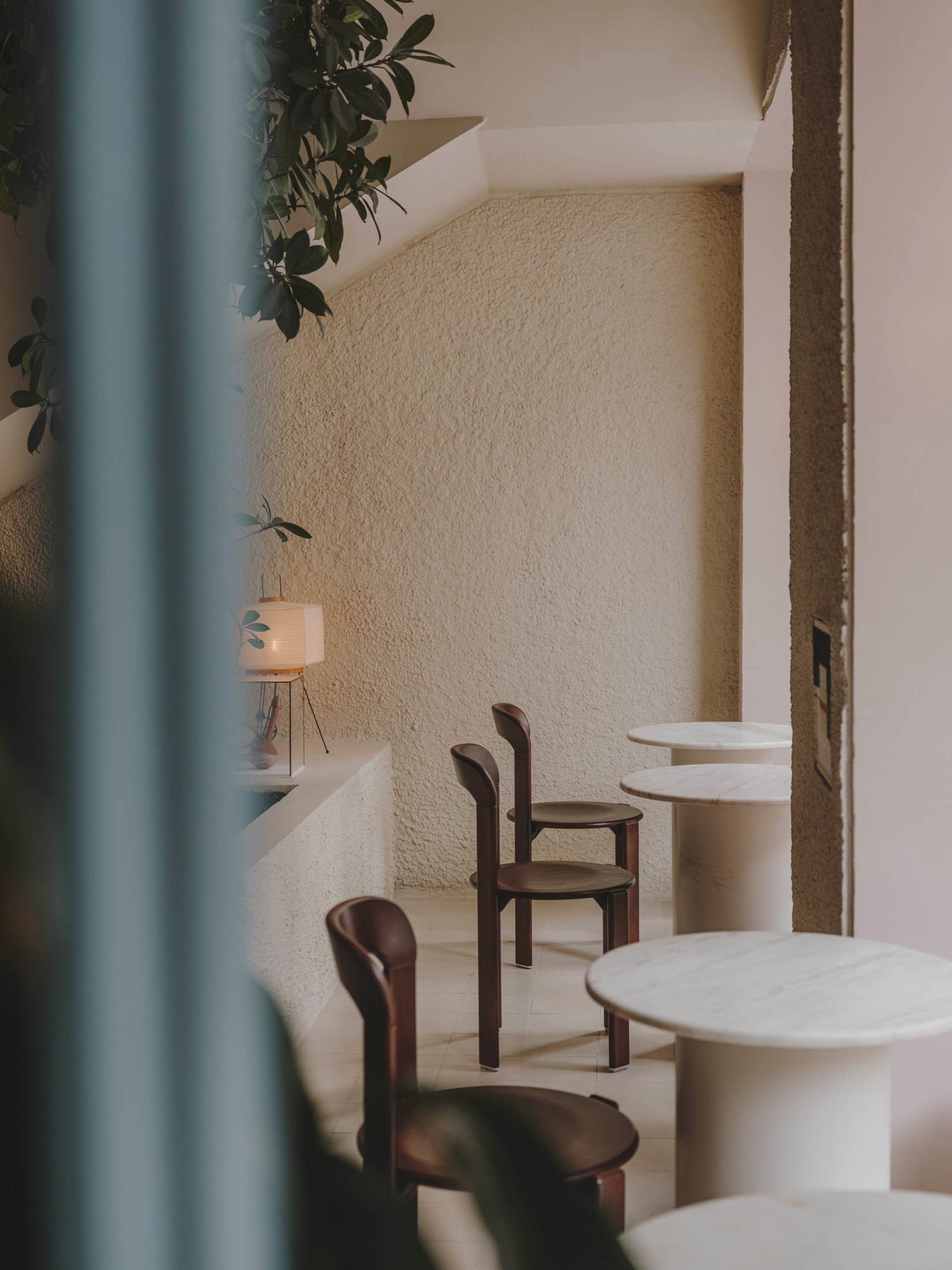 Minimalist cafe with round marble tables and wooden chairs, featuring textured walls and indoor plants.