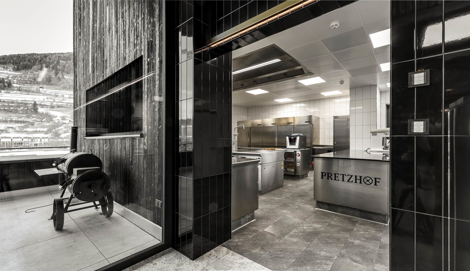 Modern commercial kitchen with stainless steel appliances and black and white tile flooring.