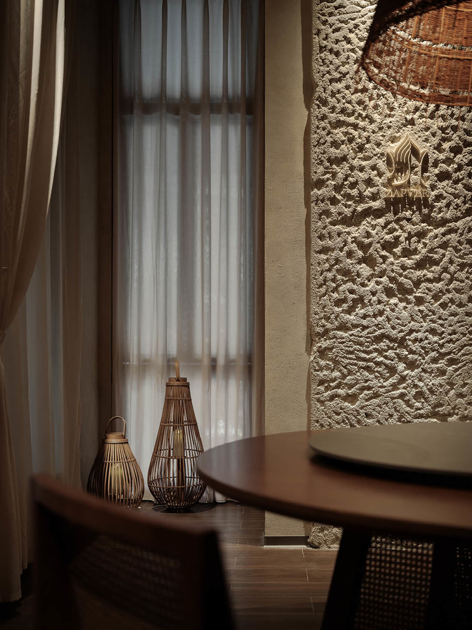 A modern restaurant interior featuring wooden textures, modern lighting, and a textured stone wall with a logo sign.