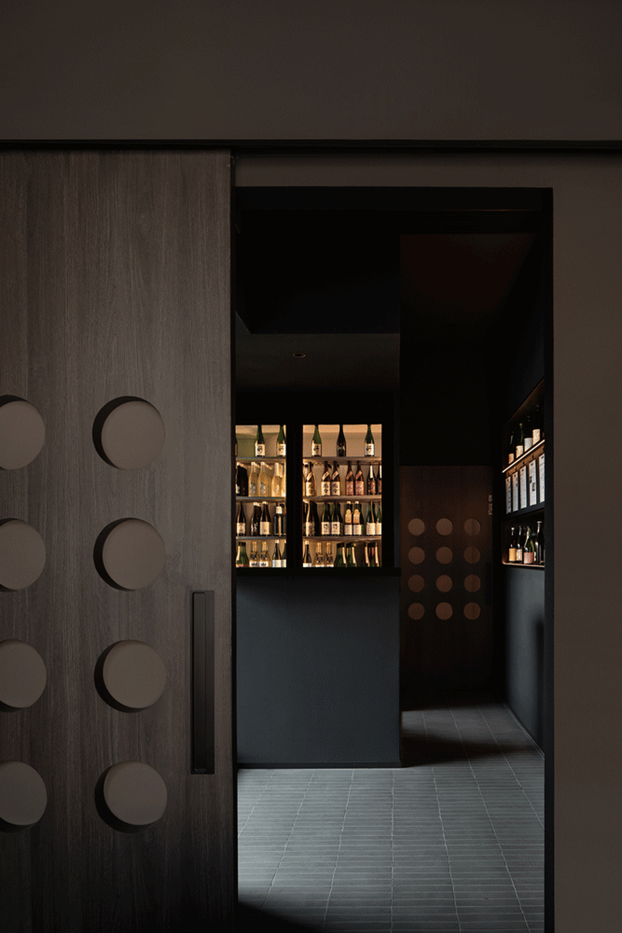 Interior of a modern wine bar with dark walls and a prominent wooden sliding door.