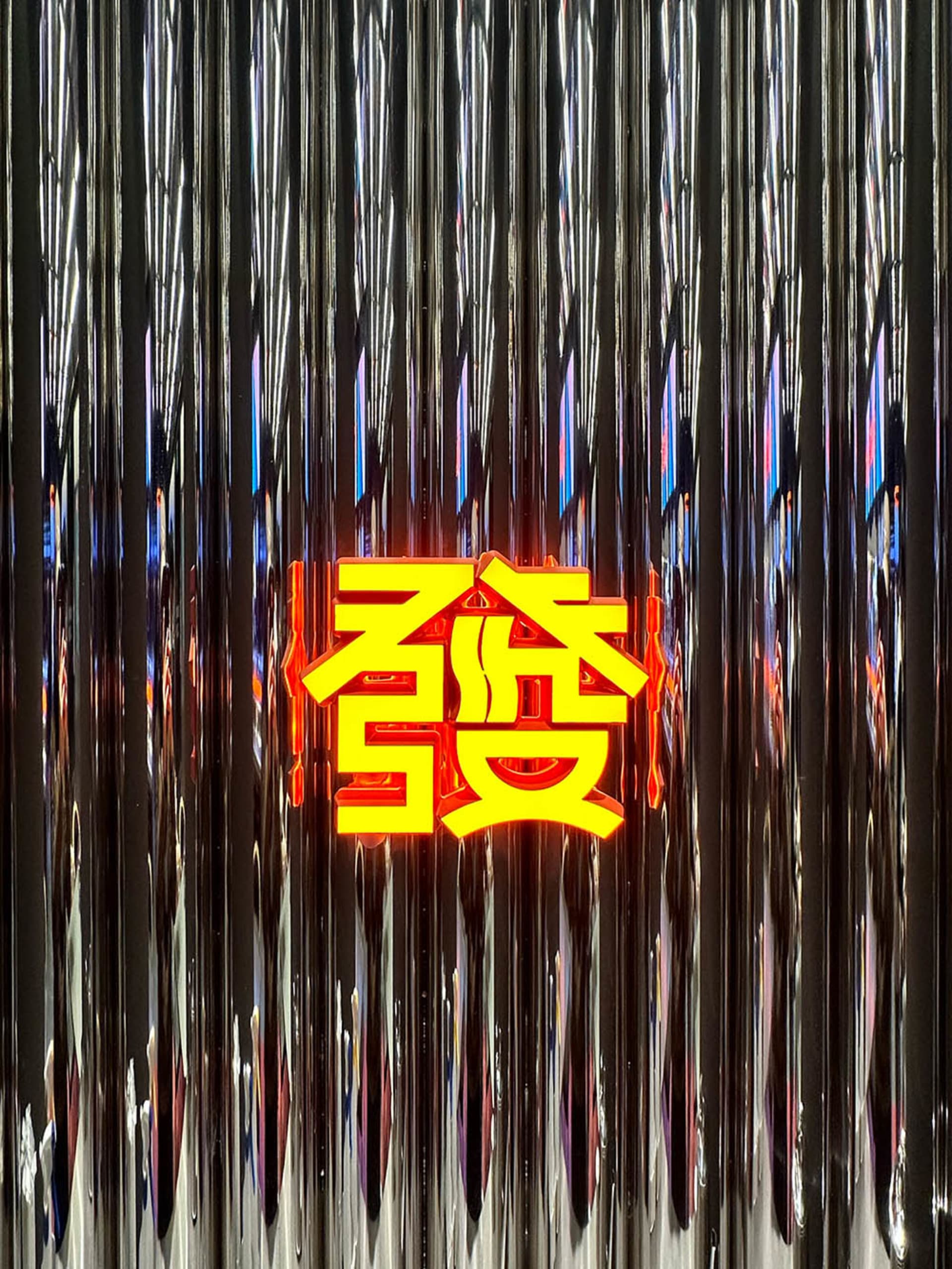A neon sign featuring the Chinese character '發' (fa), meaning 'fortune' or 'prosperity', displayed against a metallic, reflec