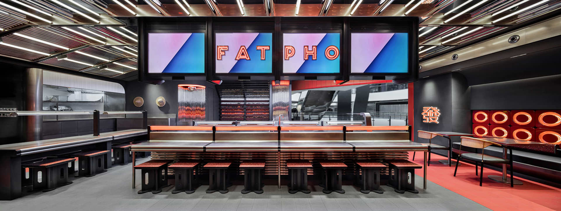 Modern, industrial-style food court interior with metal benches, wooden seating, and neon lighting.