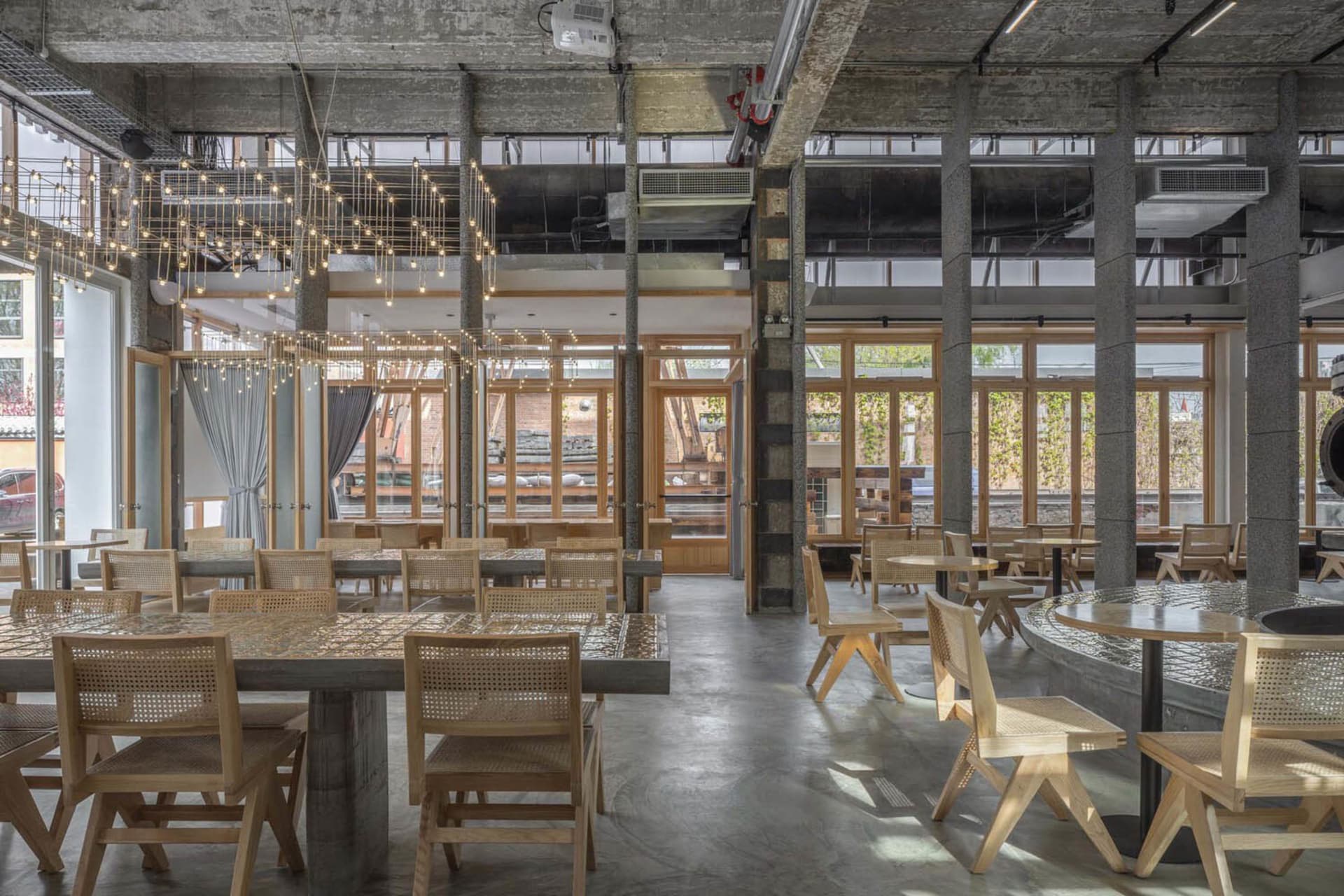 Industrial-style restaurant interior with wooden tables and chairs, concrete flooring, and glass windows.