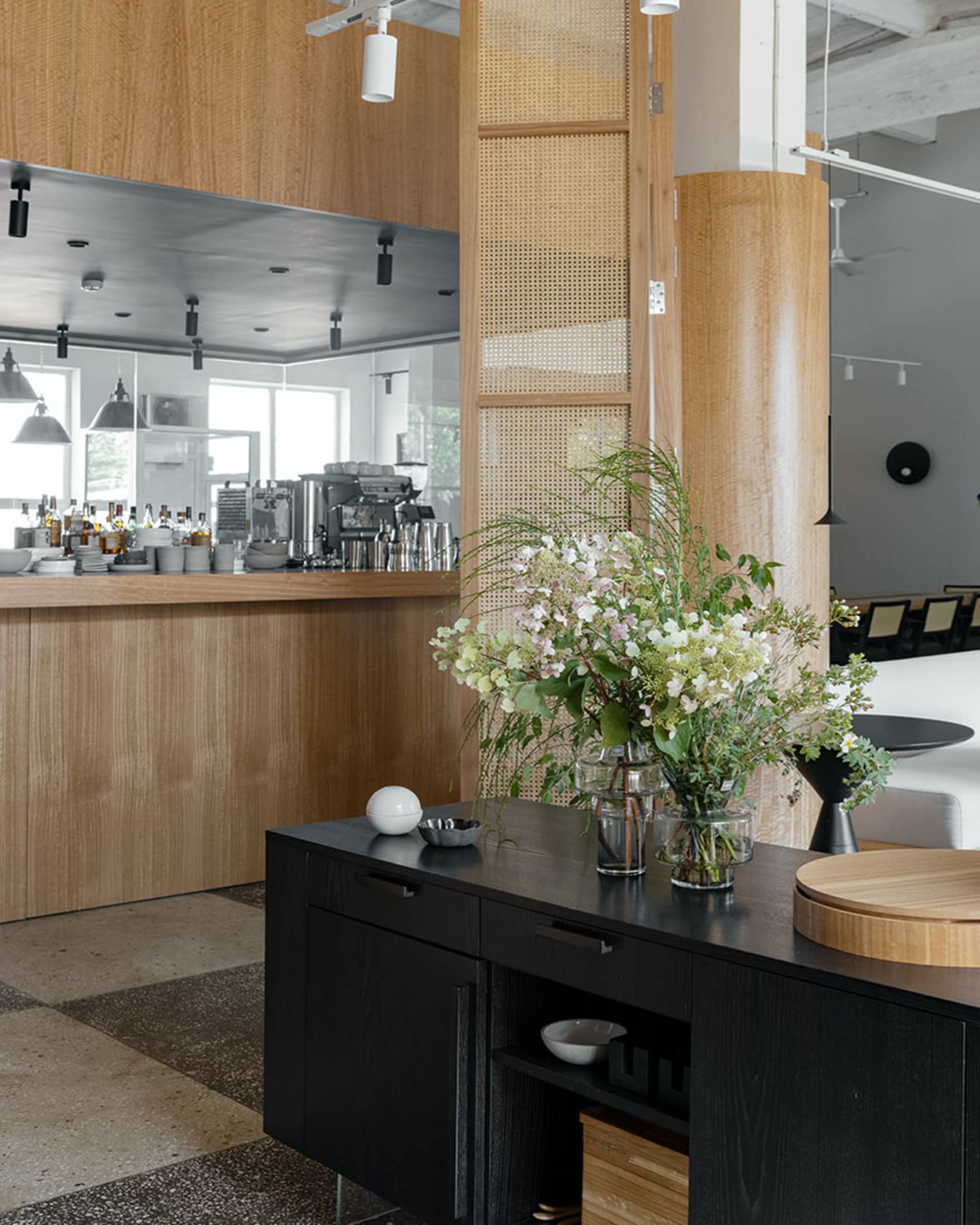Minimalist interior design featuring a wooden counter with a vase of flowers and a coffee bar in the background.