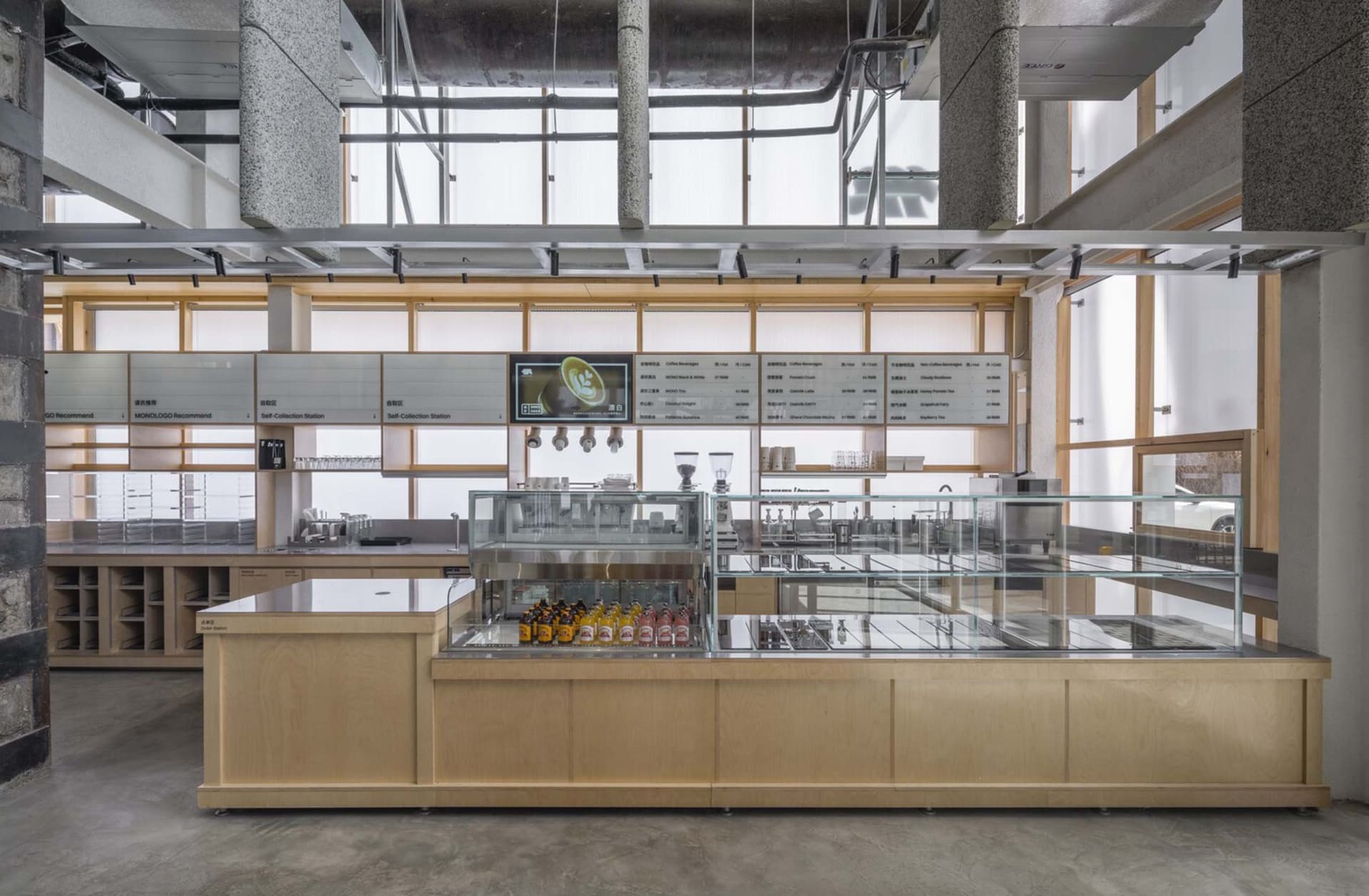 Modern industrial-style coffee shop with wooden counter, steel accents, and glass display cases.