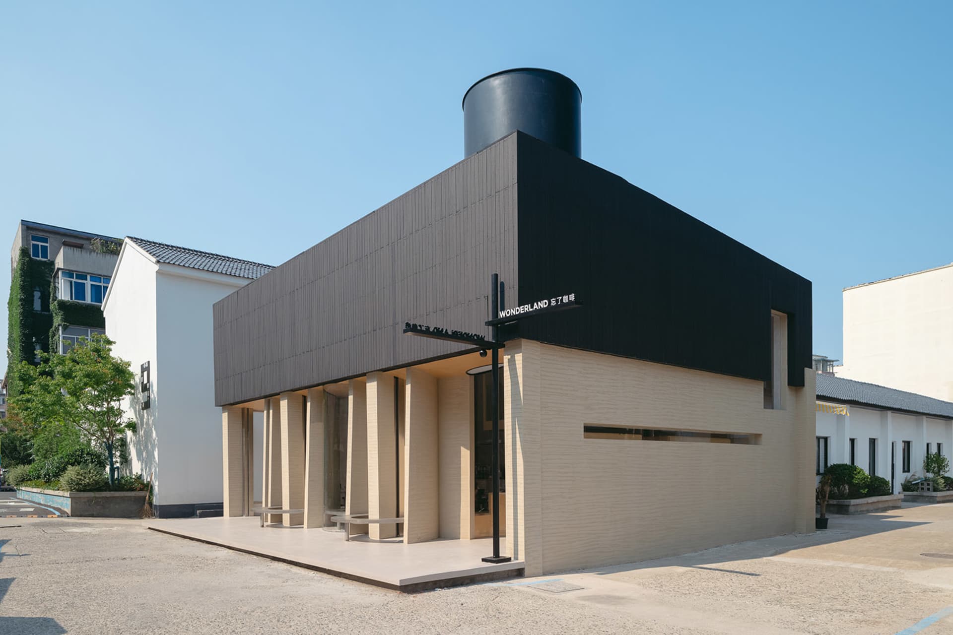 A modern, minimalist coffee shop with a concrete exterior and a large, black cylindrical roof vent.