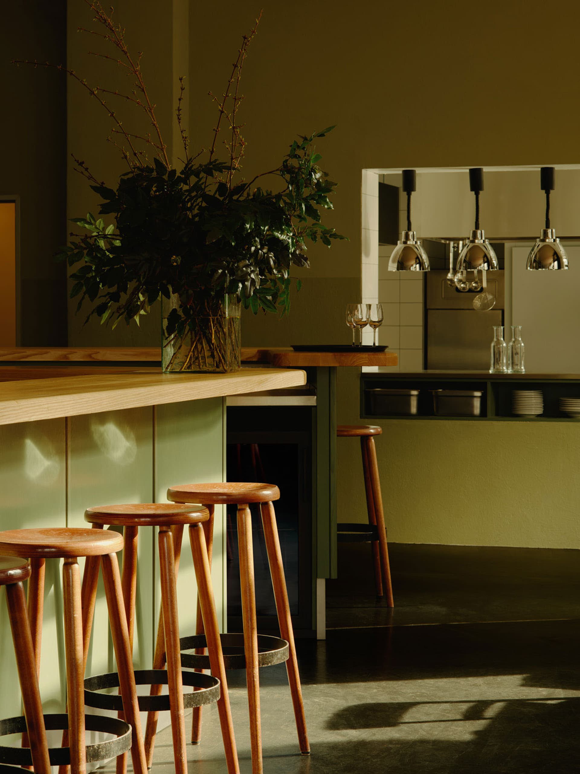 A modern kitchen with wooden stools, green cabinets, and a vase of flowers.