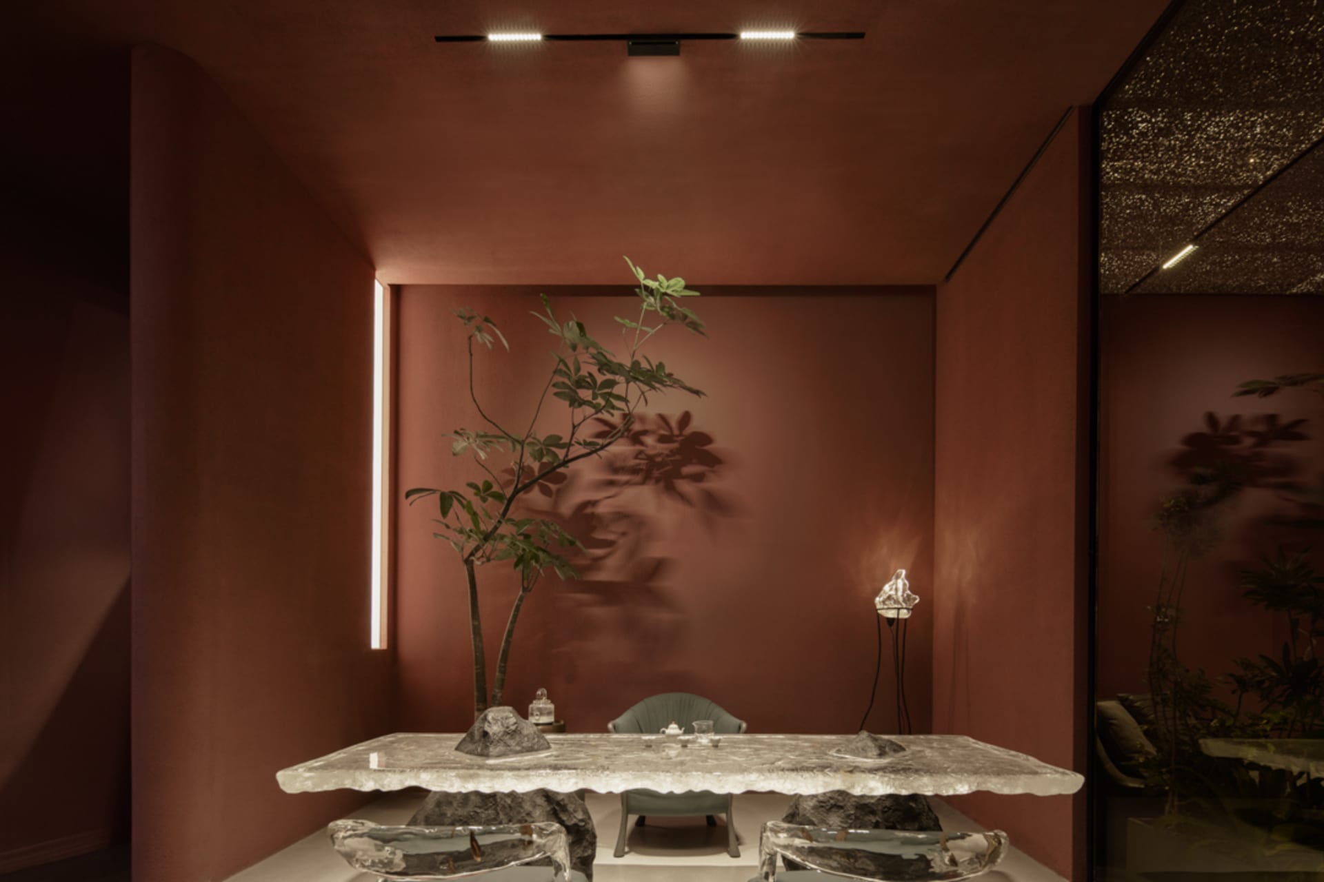 Modern restaurant interior with a glass table, greenery, and minimalist lighting.