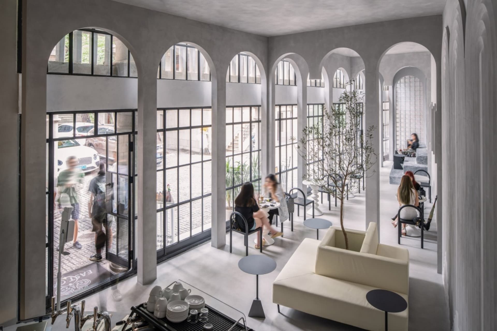 An industrial-style restaurant interior with concrete arches and large windows.