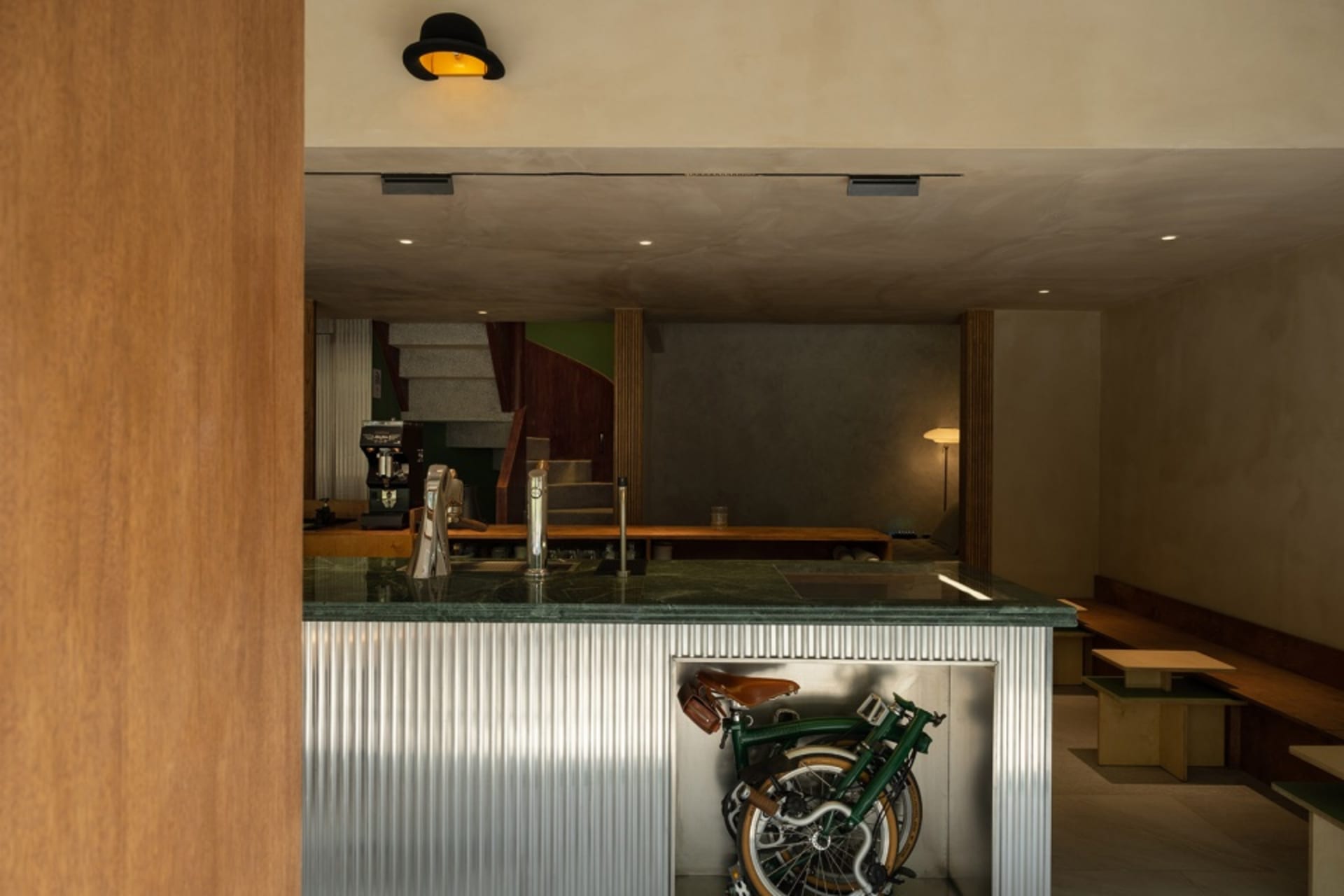A metallic folding bike is stored under a modern coffee shop's counter.
