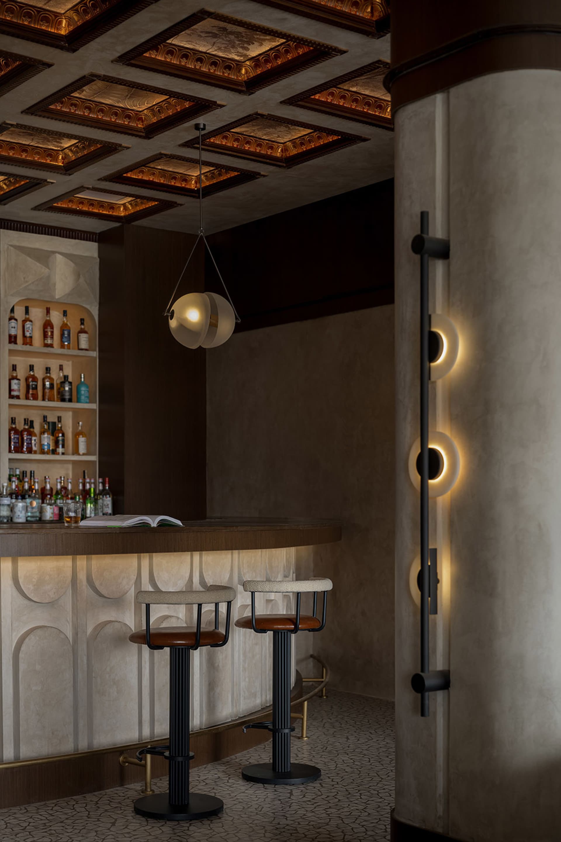 Modern bar area featuring a concrete counter with a metal railing and wooden bar stools.