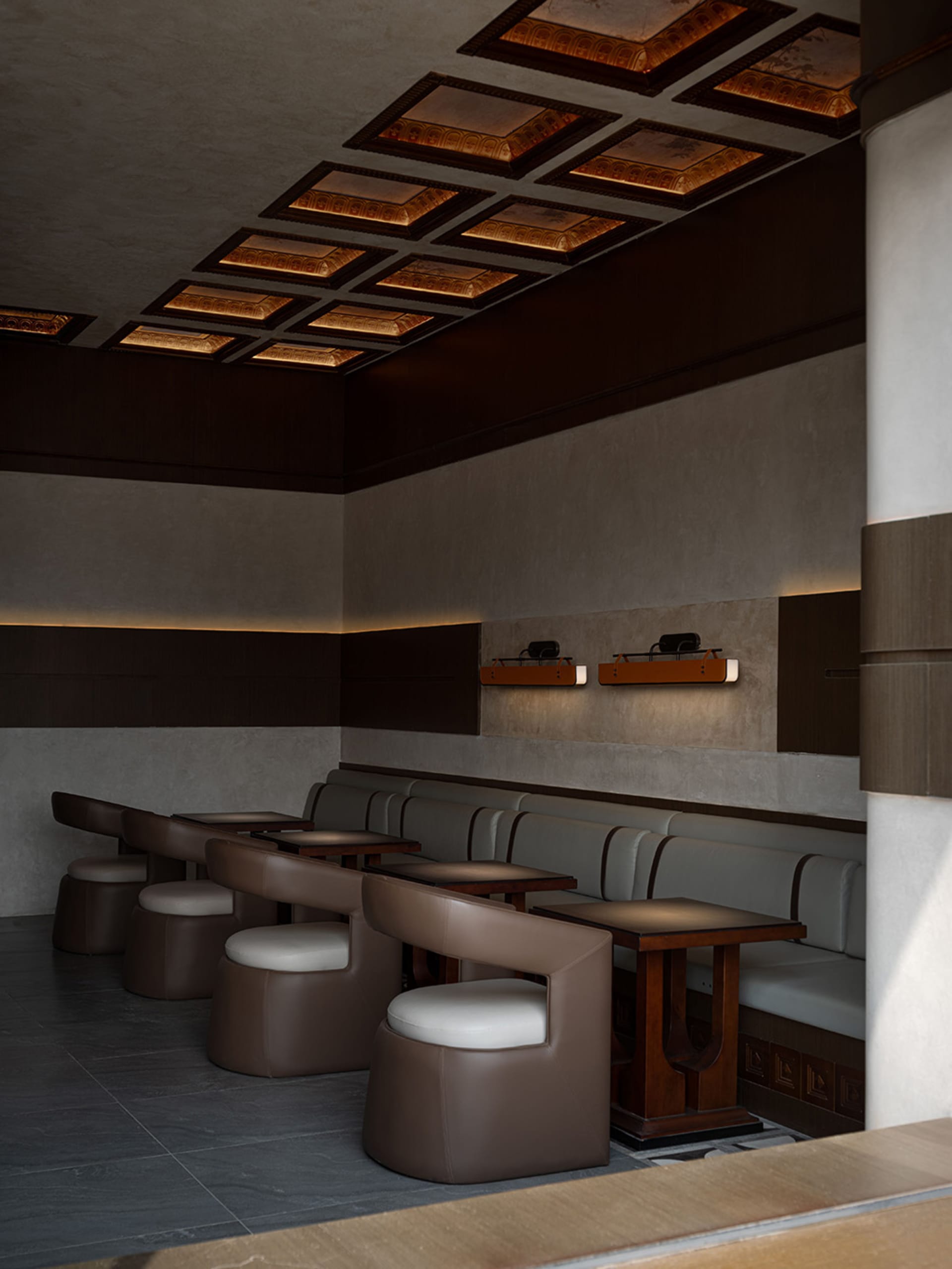Modern, minimalist restaurant interior with sleek leather chairs, wooden tables, concrete walls, and recessed lighting.