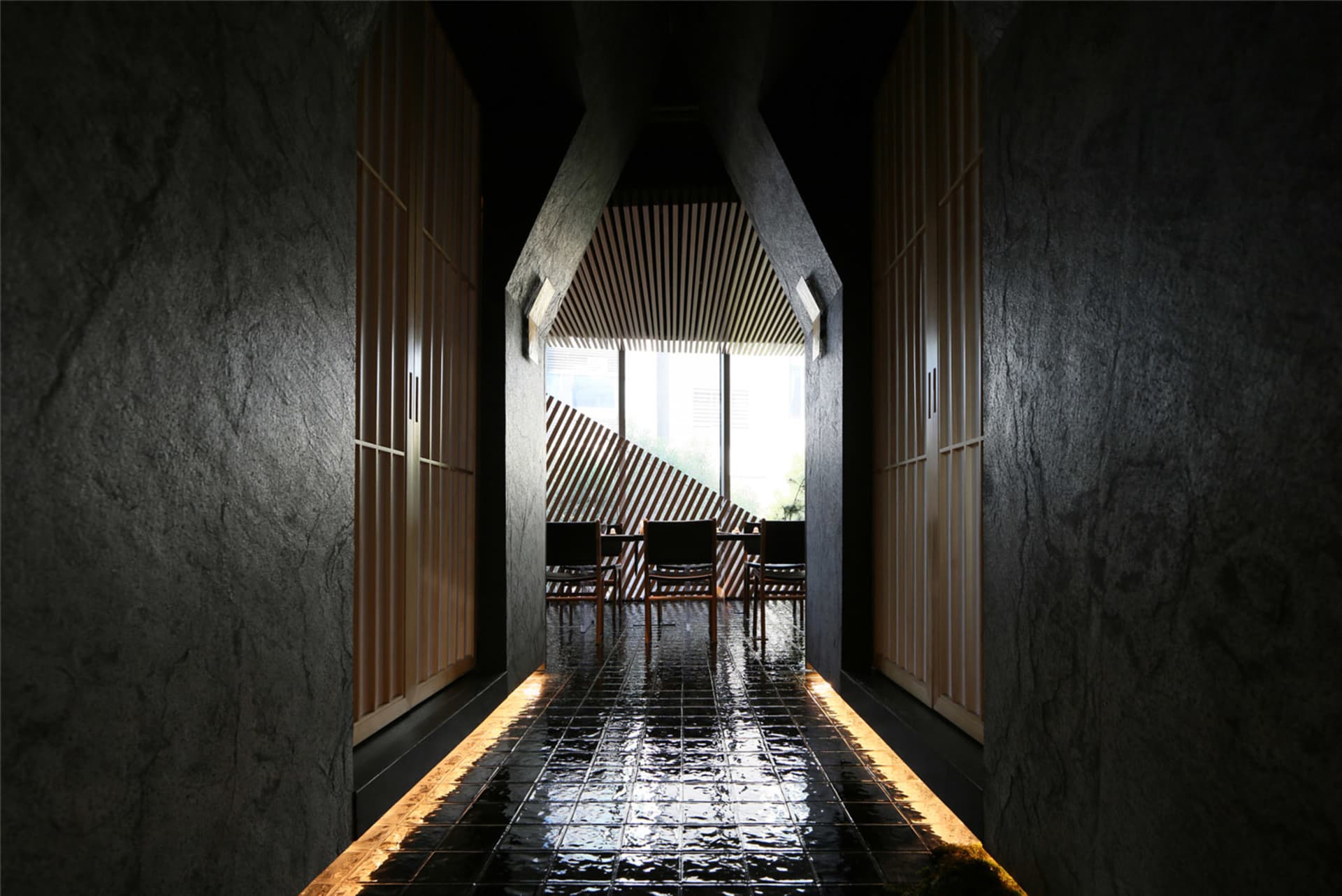 A minimalist waiting area with concrete walls, wood furniture, and a view through a tall window.