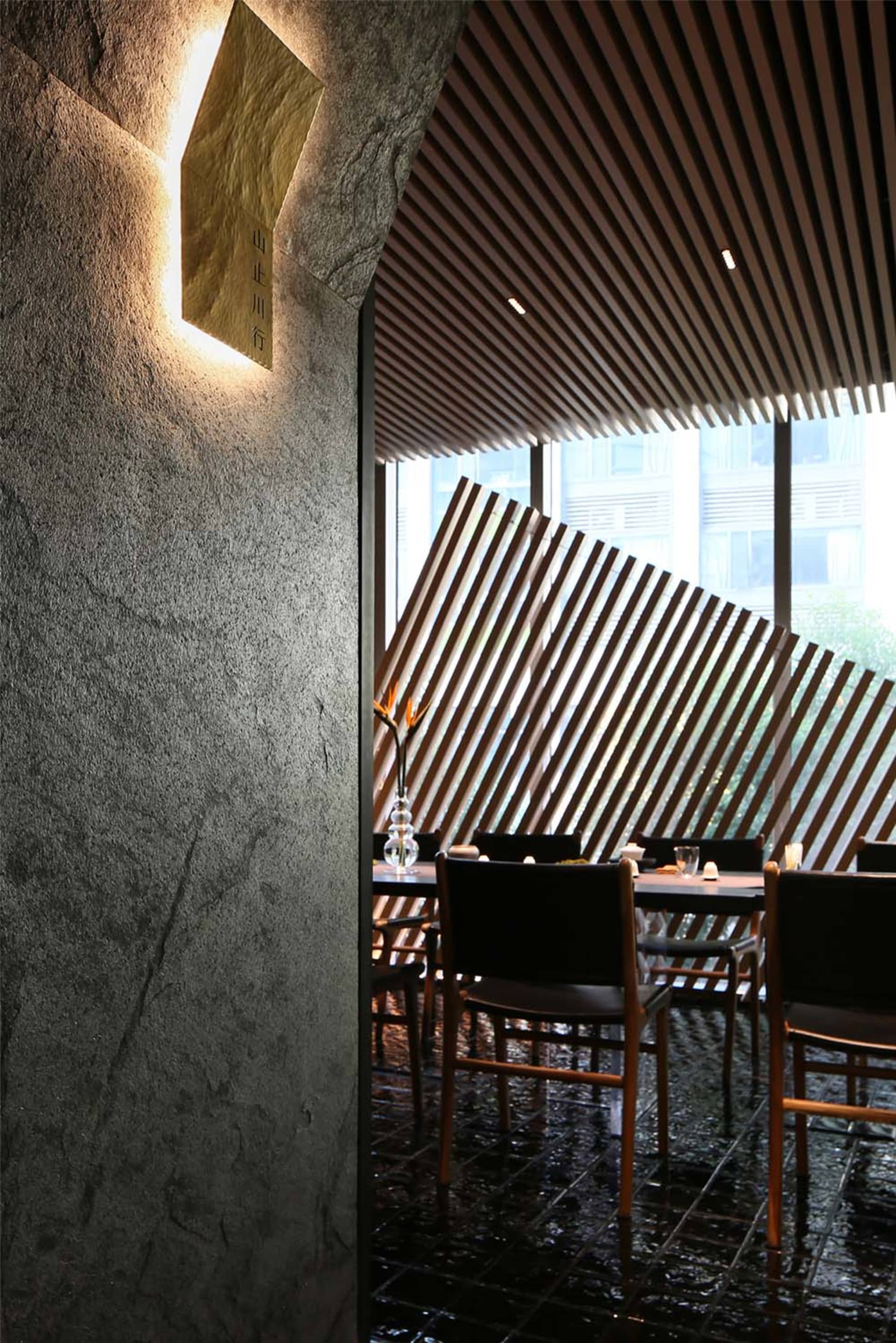 A modern restaurant interior featuring a wooden wall and ceiling paneling with a vase on a dining table and a window with str
