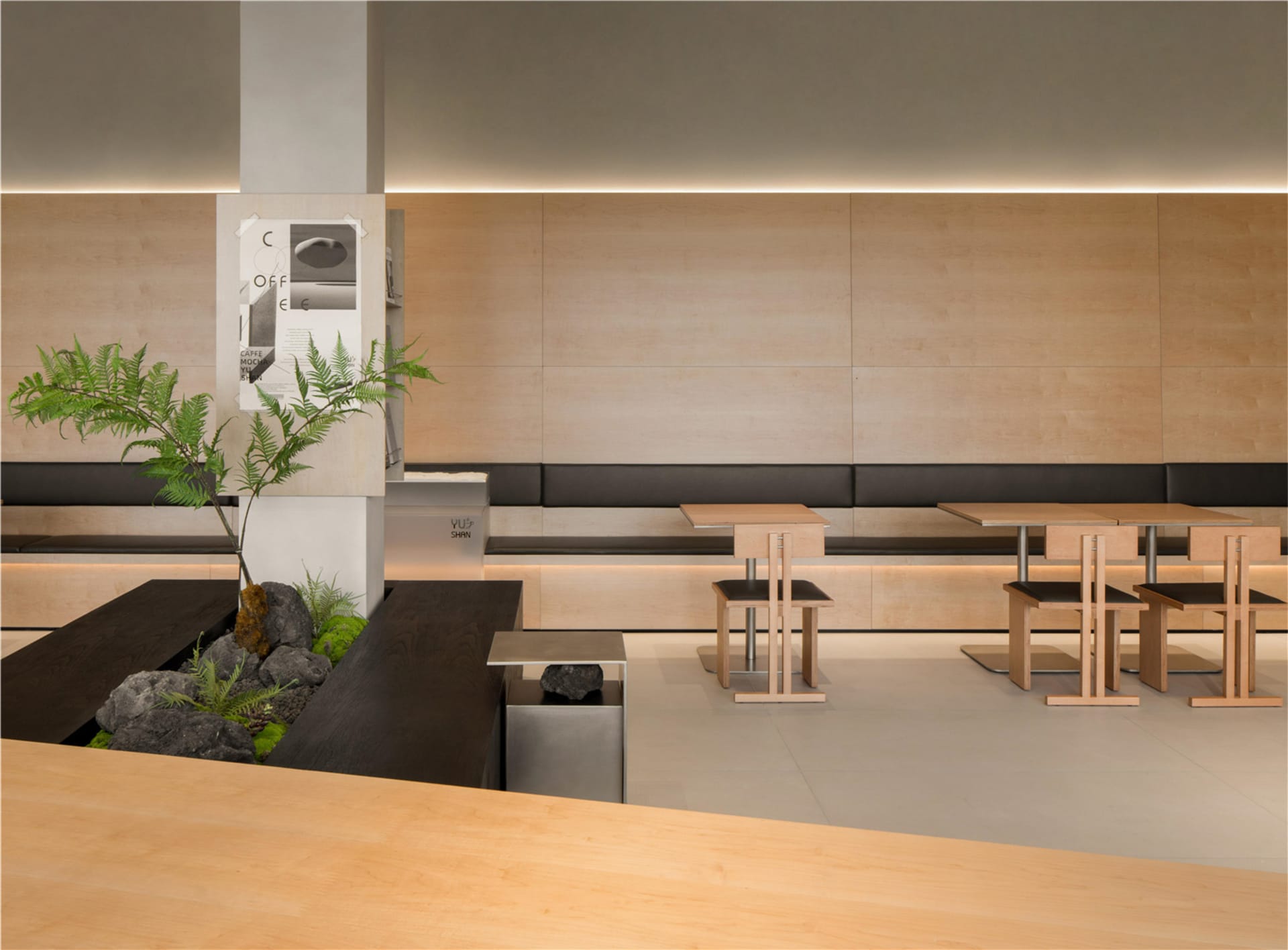 A minimalist restaurant seating area with wooden tables and chairs, featuring a plant and rock decoration.