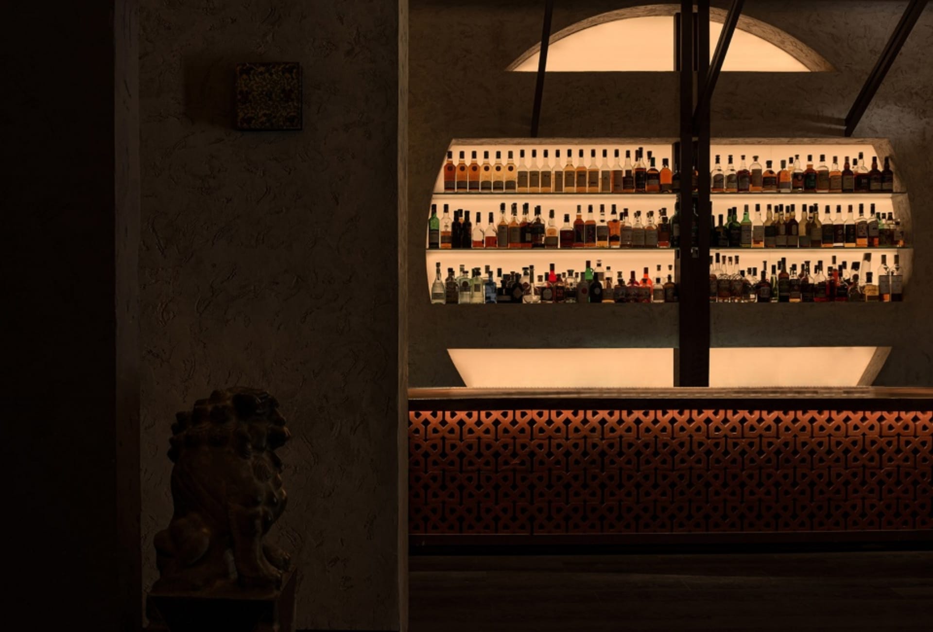 A bar interior with concrete finishes and shelves filled with bottles.