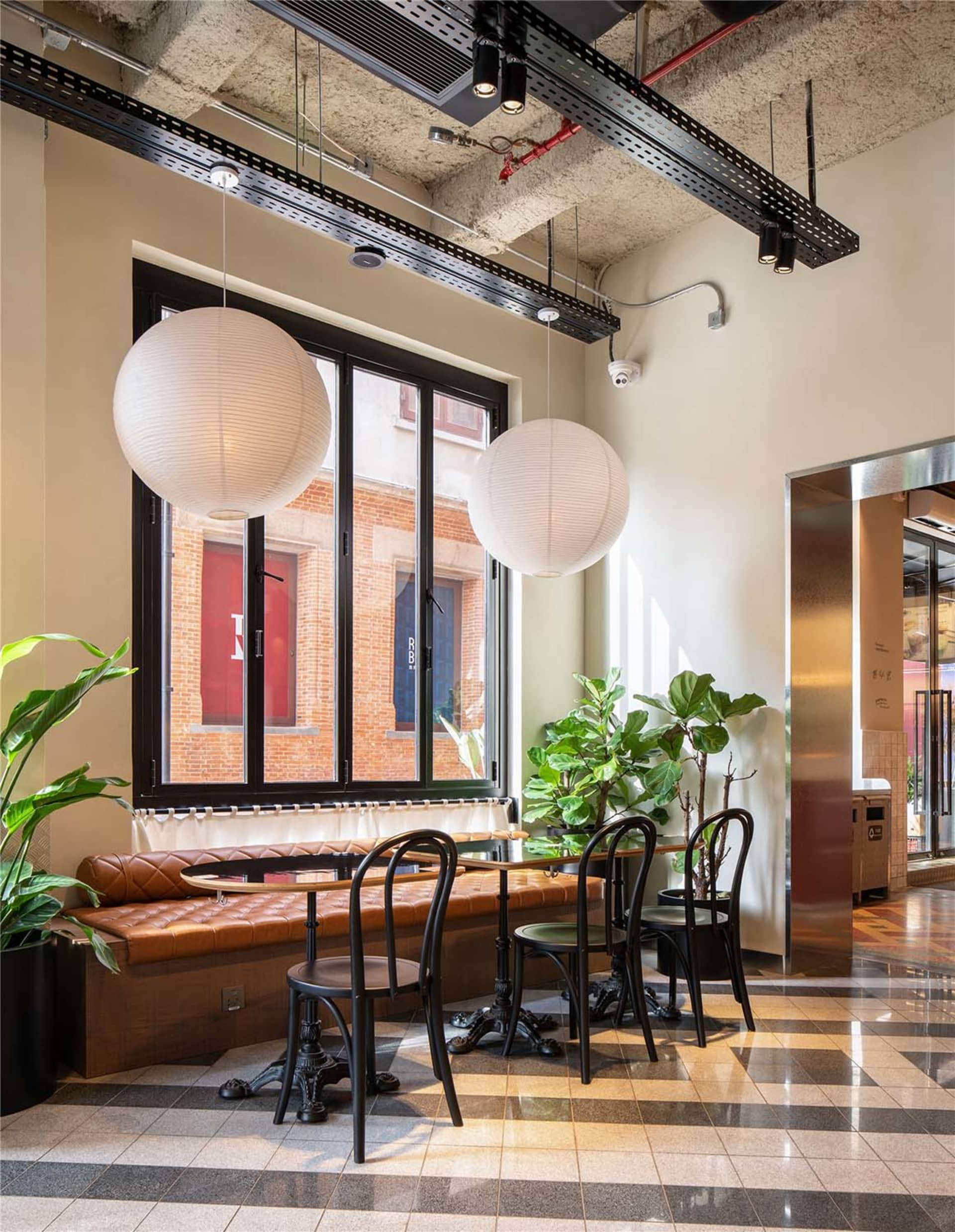 A modern industrial restaurant interior with fabric seating, metal chairs, and glass windows.