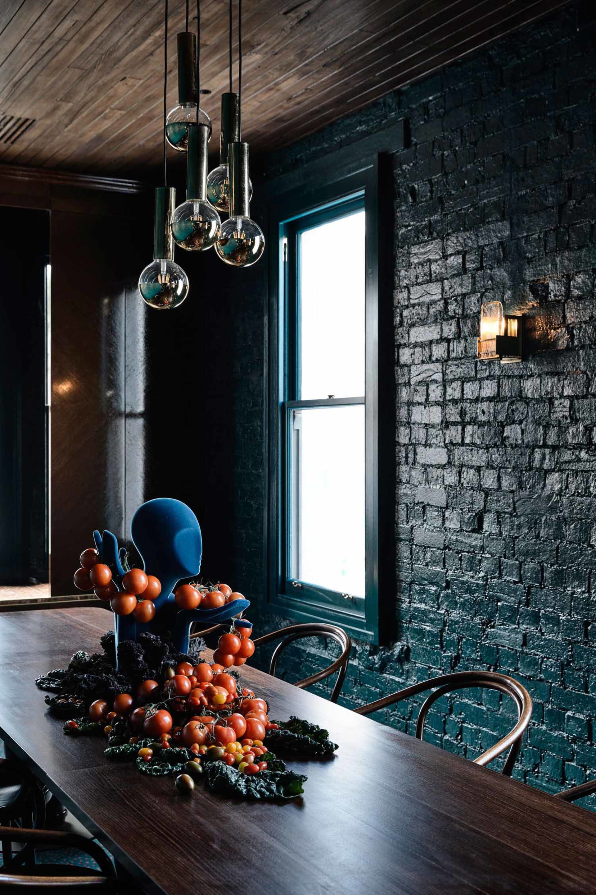 A rustic, dark wood dining room with industrial lighting and a unique centerpiece featuring tomatoes and greens.