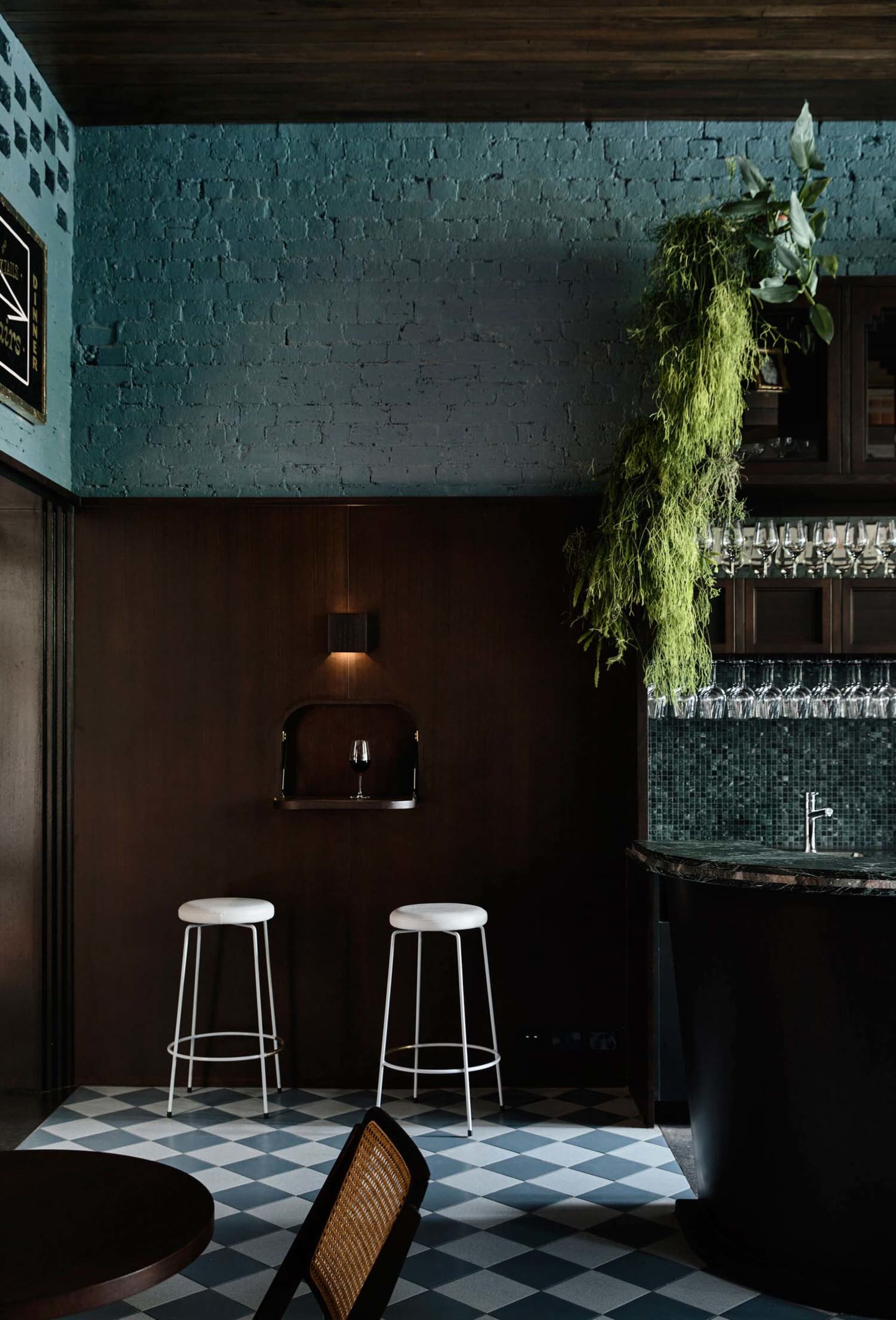 Minimalist restaurant bar with greenery hanging from the ceiling and dark wooden walls.