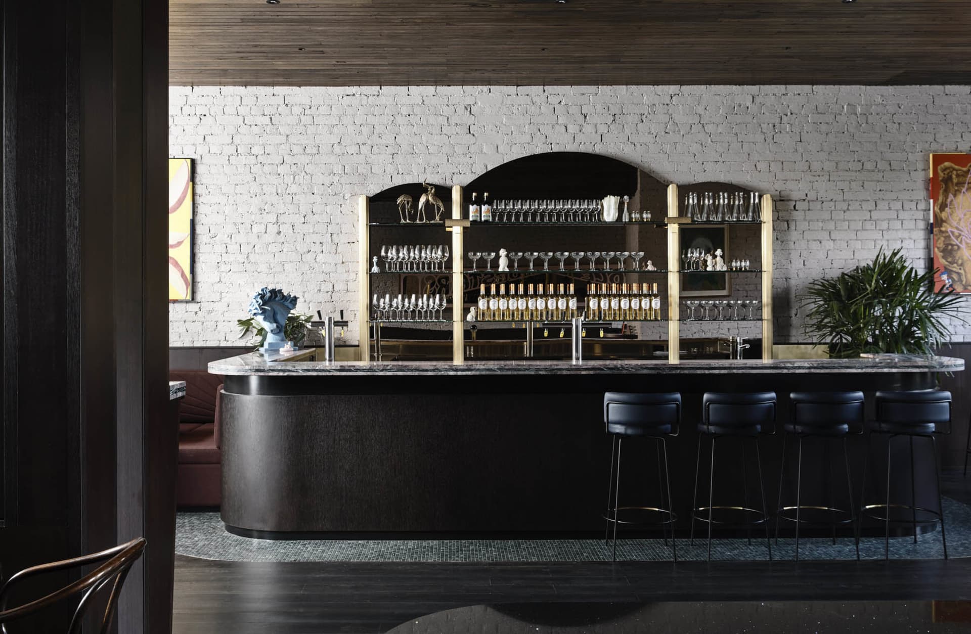 A modern bar featuring a marble counter, with drinks and glasses on shelves in the background.