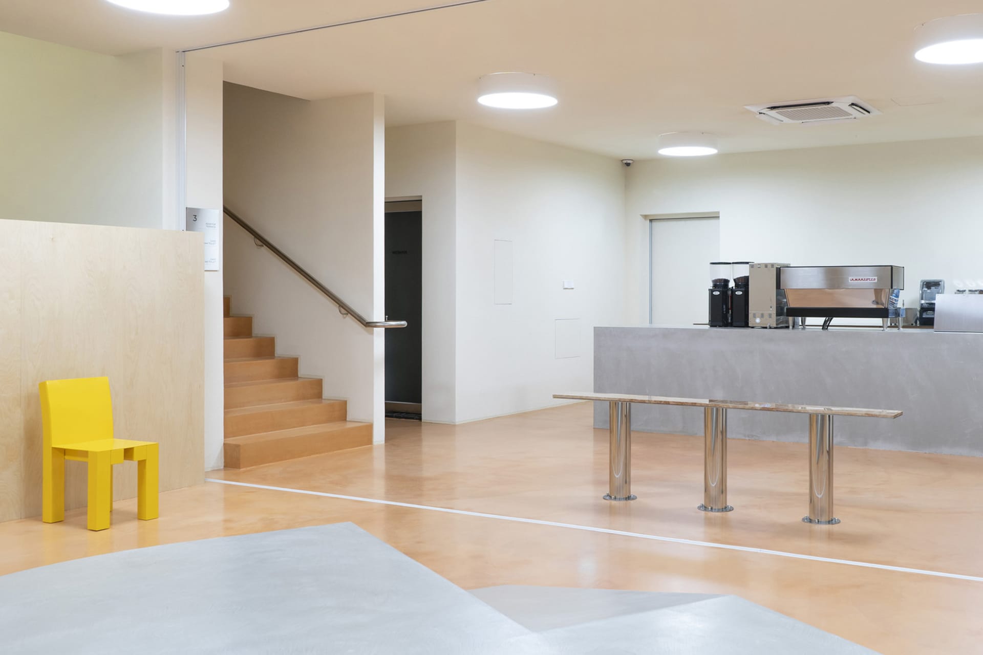 A minimalist coffee shop featuring raw concrete walls and metal accents, with sleek seating options and a modern design.