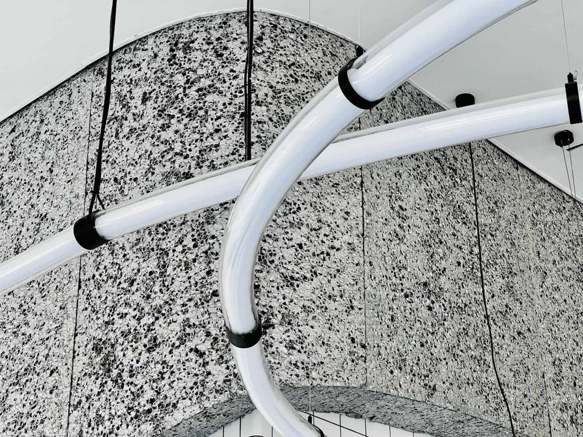White metal pipes suspended from the ceiling in an industrial setting with concrete walls.