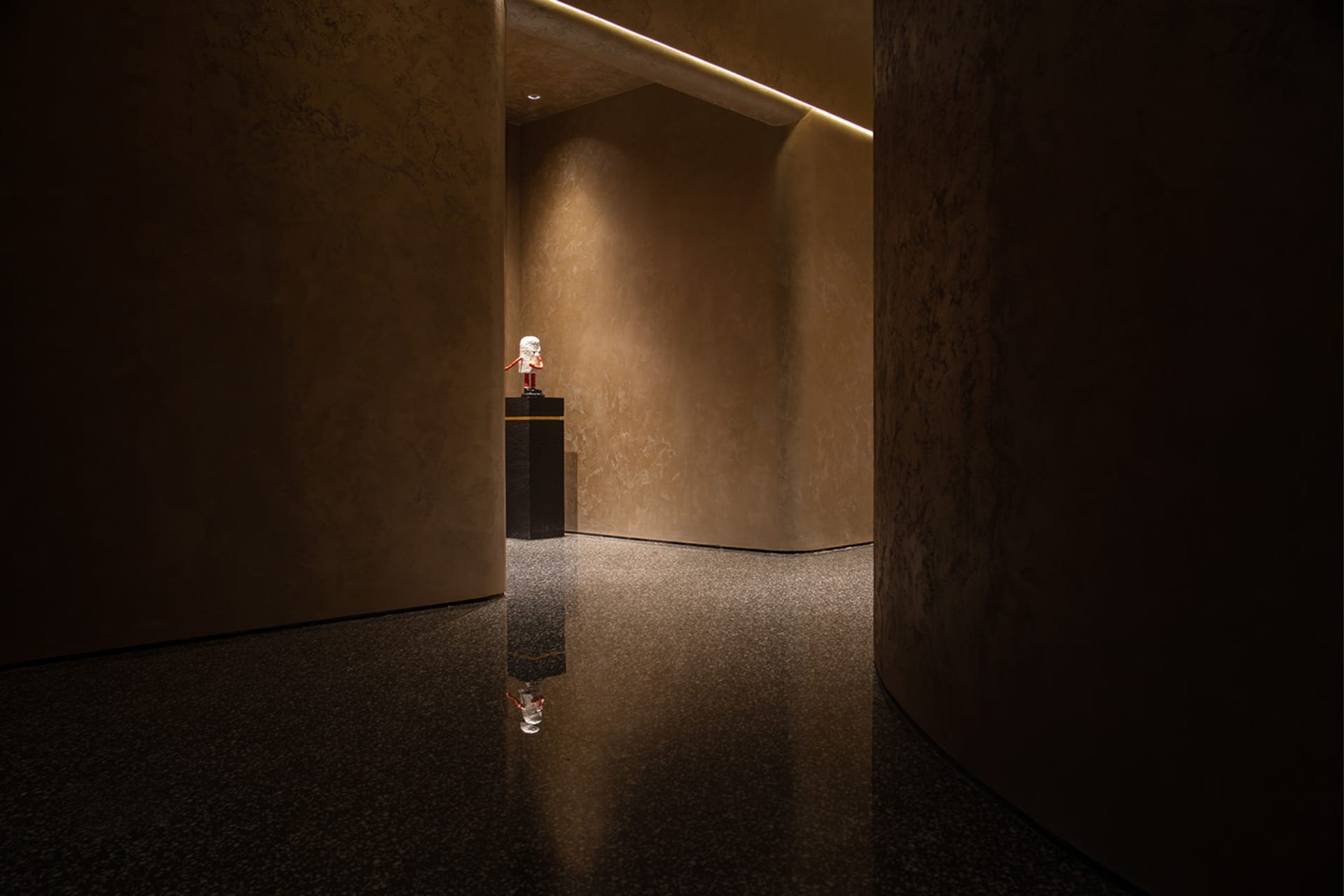 A modern hall with concrete walls and floor, featuring a small statue on a pedestal.