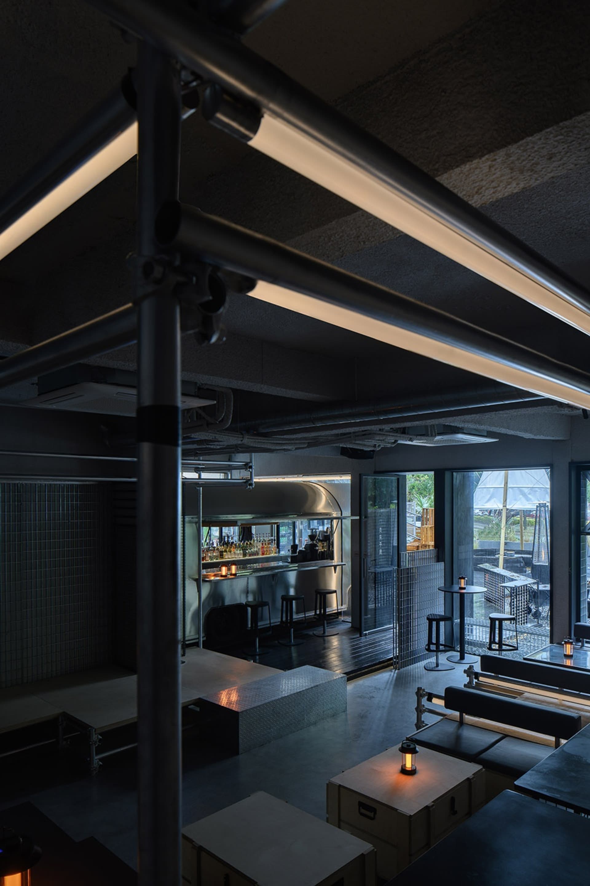 Metallic industrial-style restaurant and bar interior with exposed piping and concrete flooring.