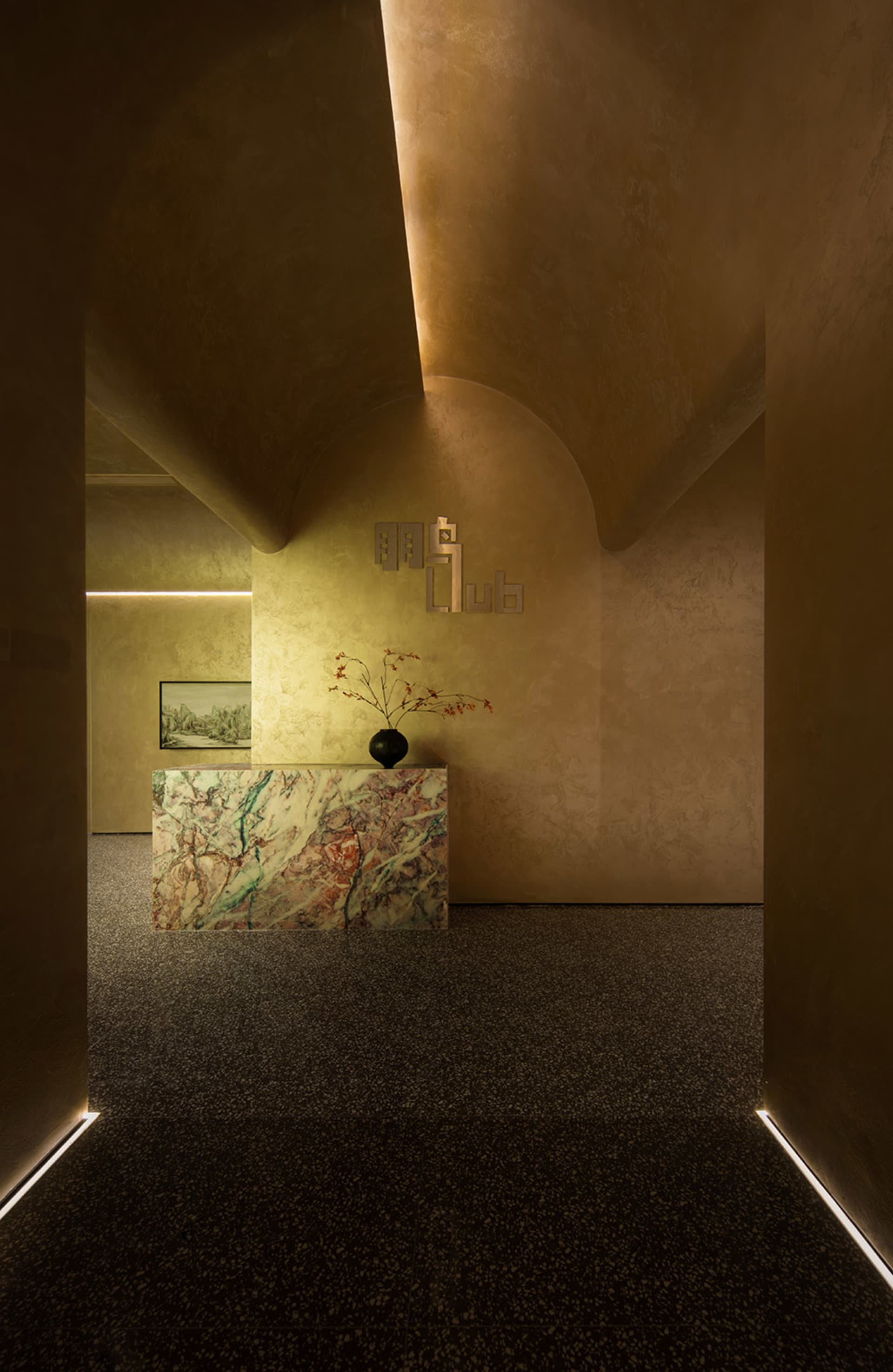 A minimalist lobby featuring a marble counter, floral arrangements, and warm lighting.