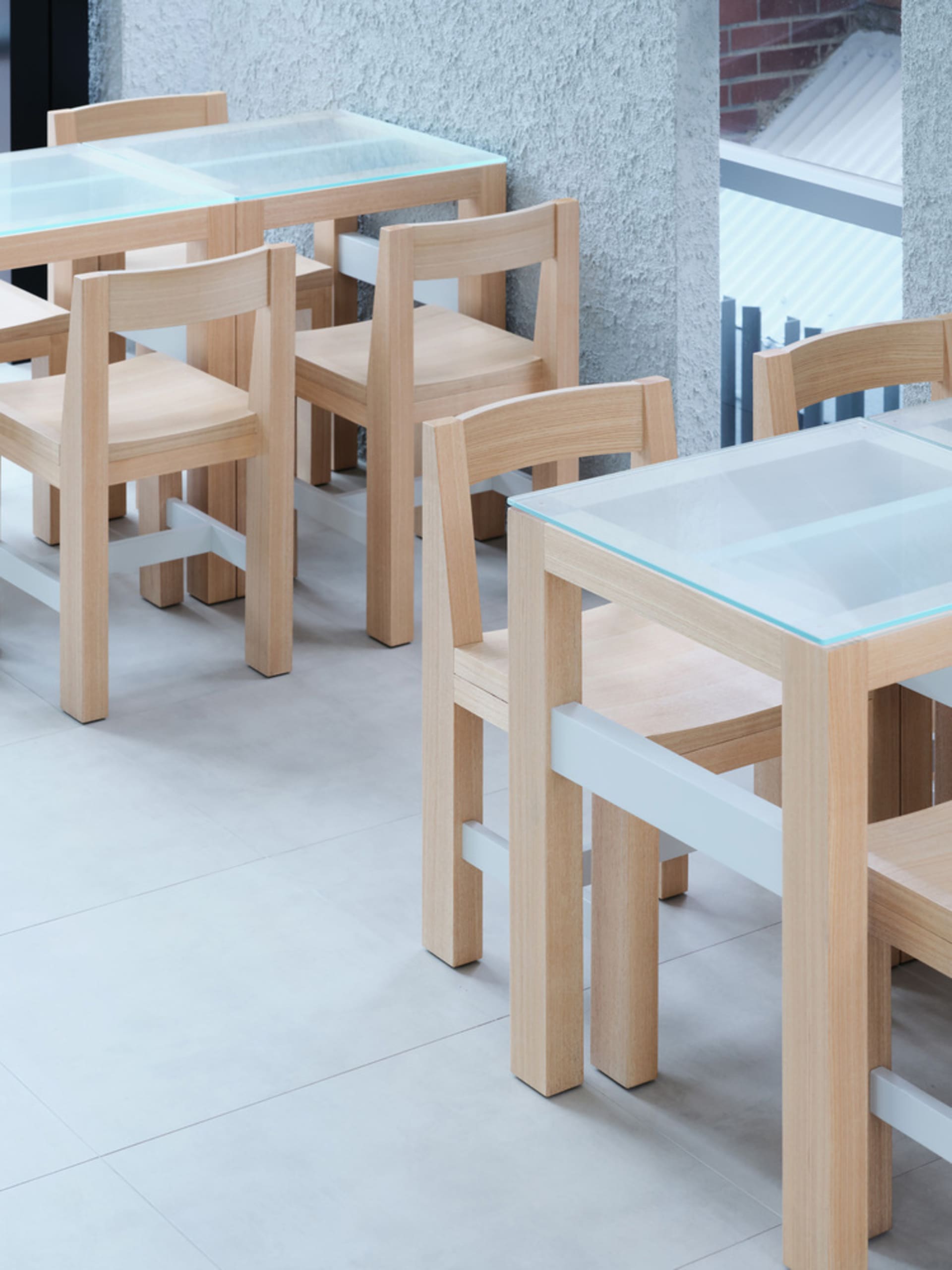 Industrial-style restaurant interior featuring wooden chairs and tables with glass tops.