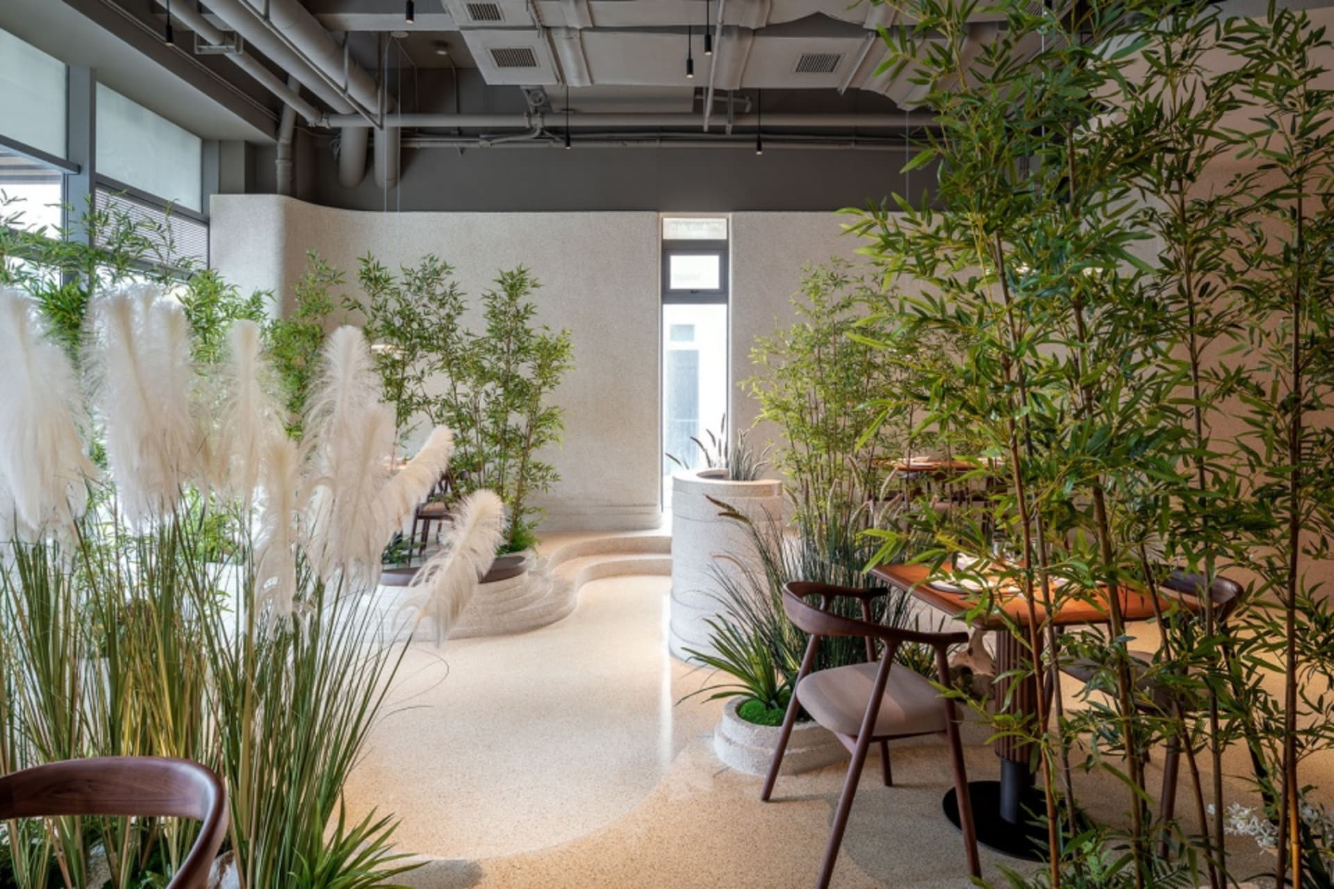 A modern restaurant interior with natural elements such as pampas grass, bamboo plants, and stone surfaces.