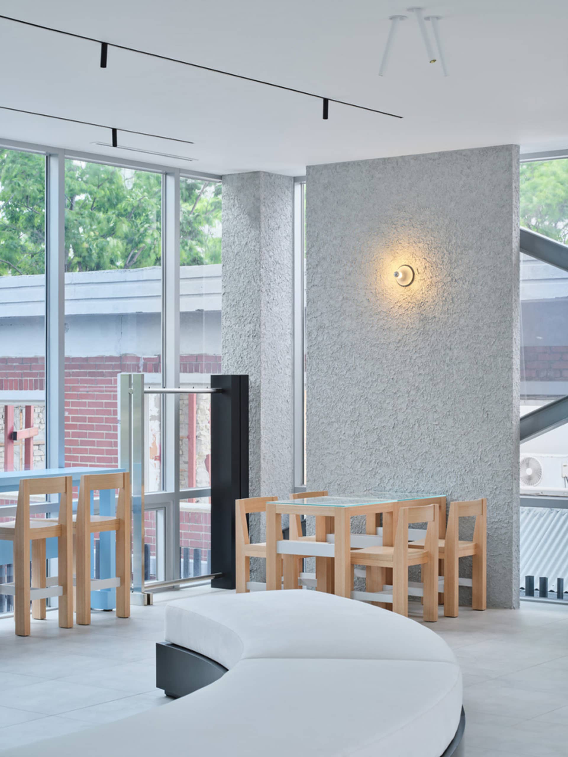 極簡餐廳室內,配有玻璃餐桌、木質餐椅,以及混凝土質感牆面。
