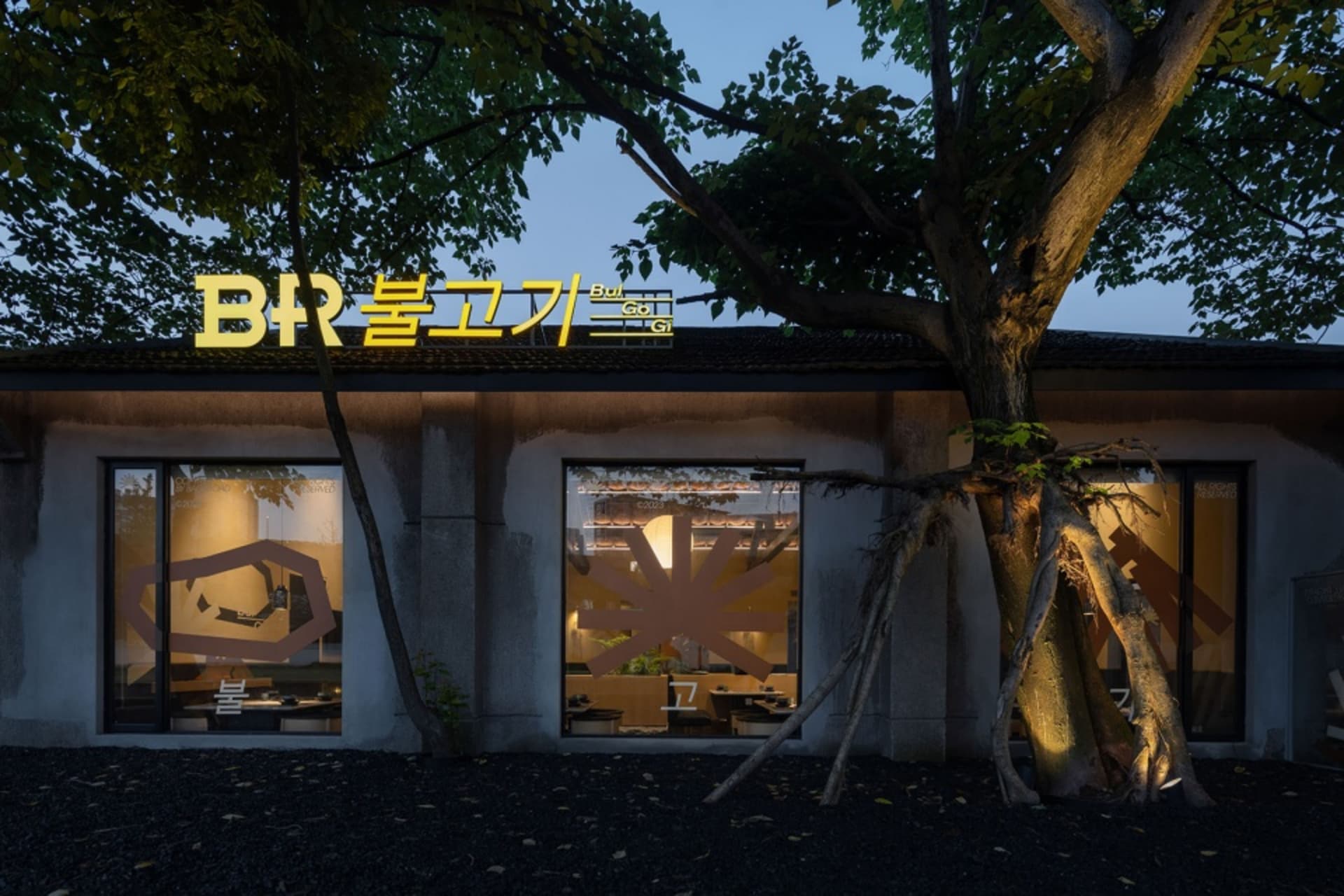 現代餐廳以玻璃牆與混凝土外觀為特色，搭配黑色土壤與一棵樹