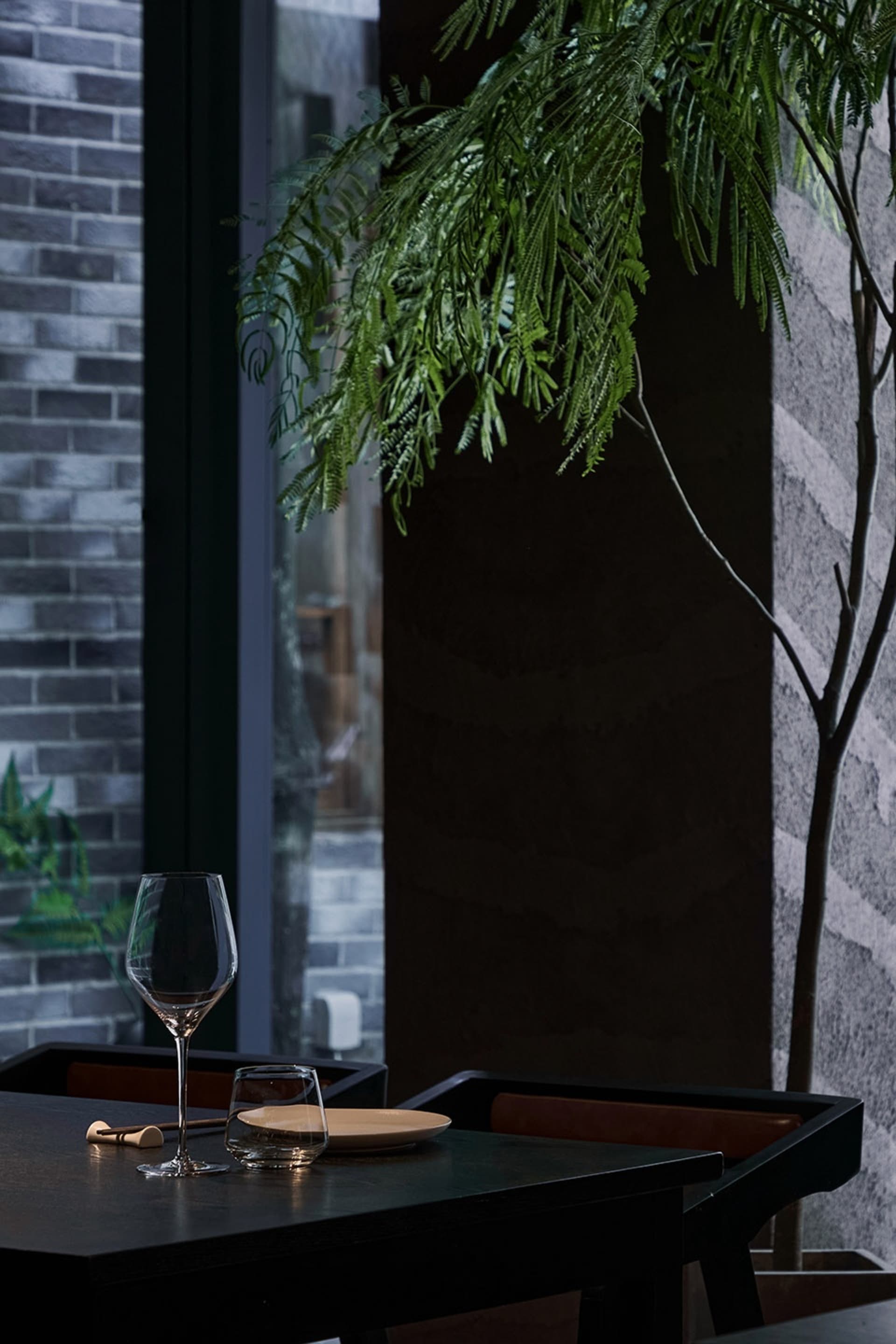 工業風餐廳內,一張俐落黑色餐桌擺放植物、玻璃杯與陶瓷餐盤。