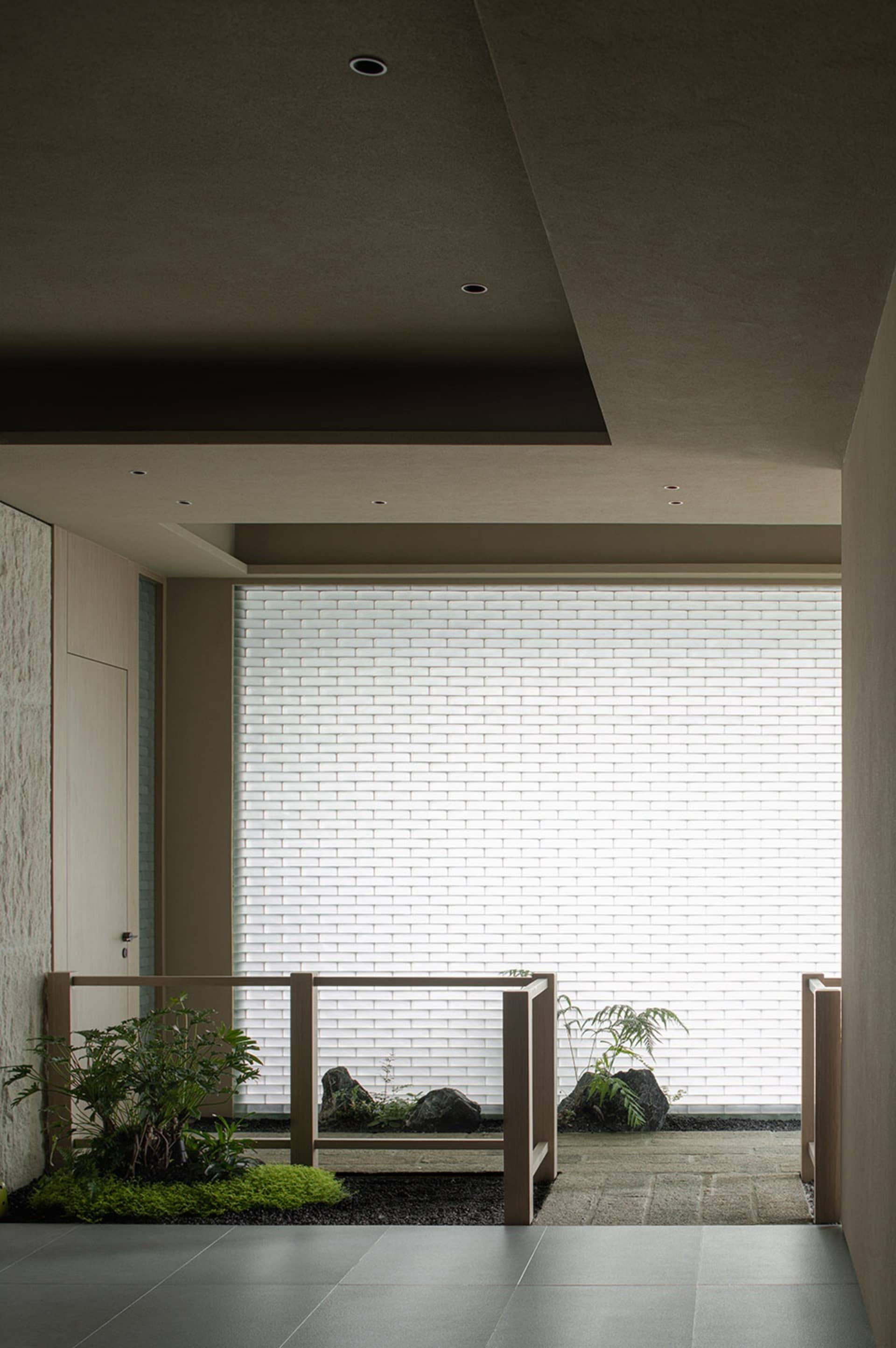 A minimalist interior with a concrete floor and walls, featuring a white brick window wall and plants.
