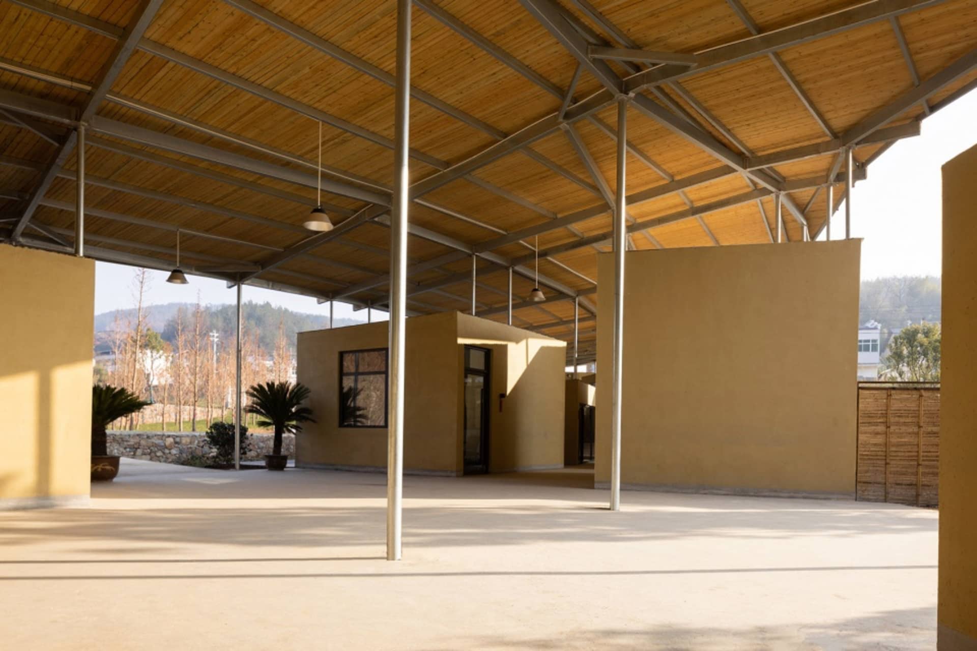 Industrial outdoor space featuring a wooden canopy, concrete floors, and metal structures.