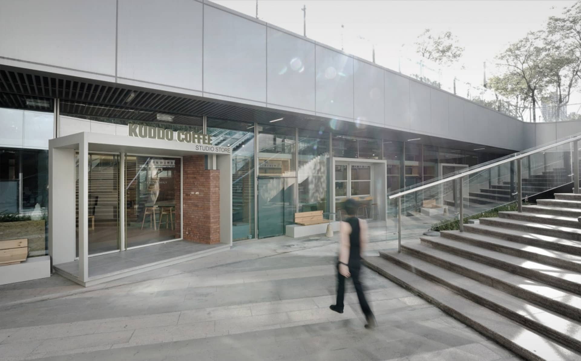A modern coffee shop storefront with a glass facade and a man walking past.