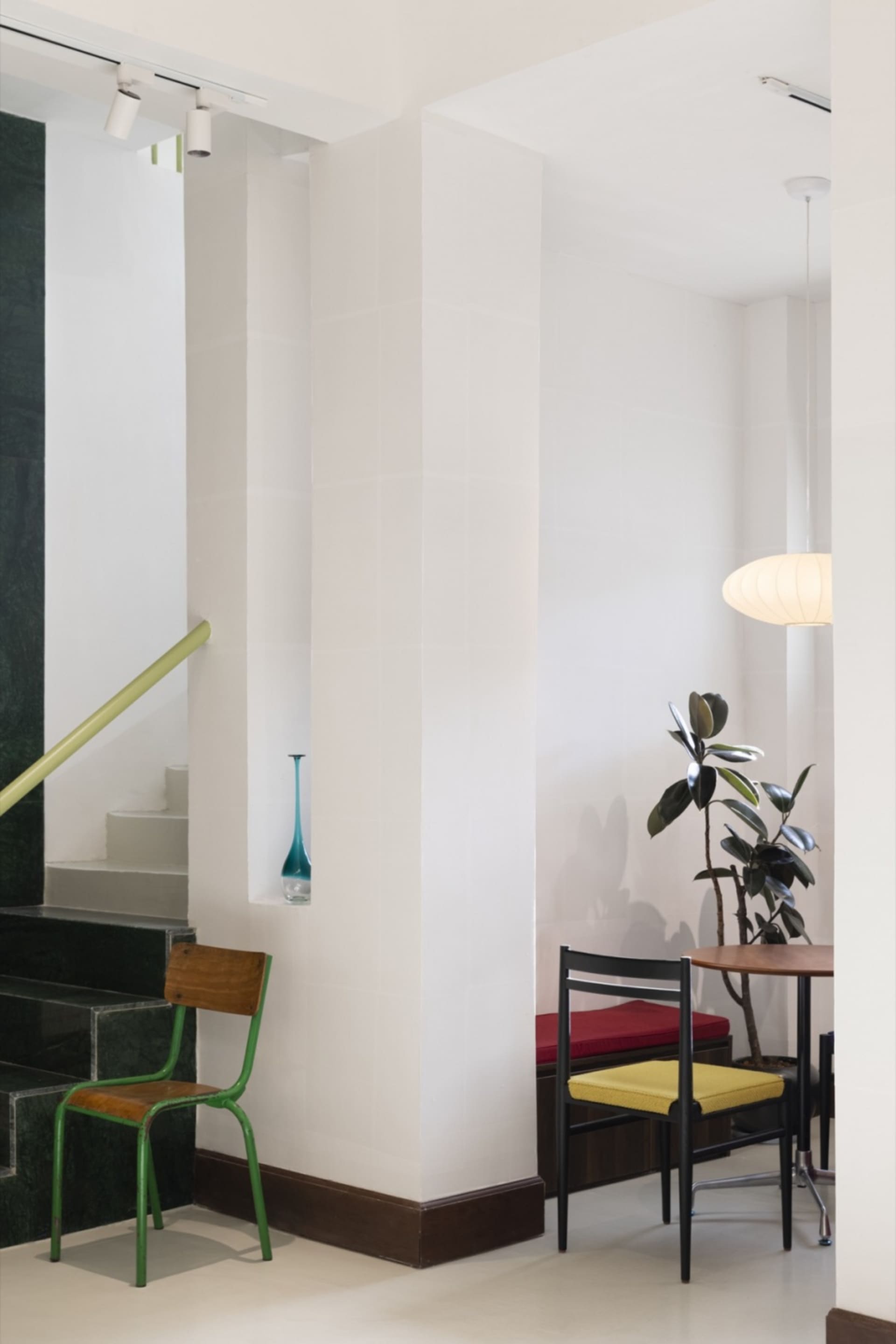 A modern restaurant interior featuring white tiles, wooden benches, and green metal accents.
