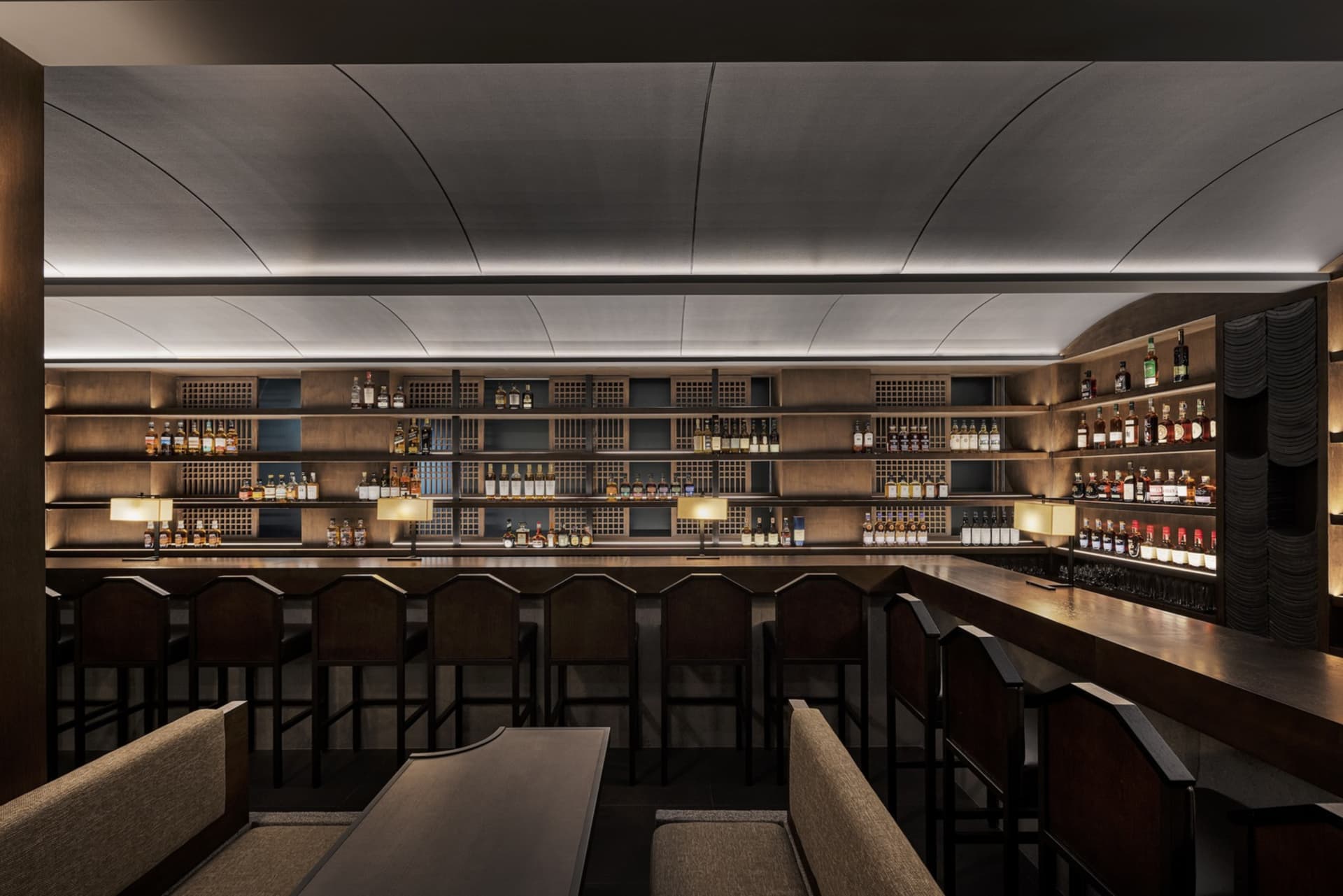 A modern restaurant bar showcasing wooden interiors and a wide selection of liquor bottles.