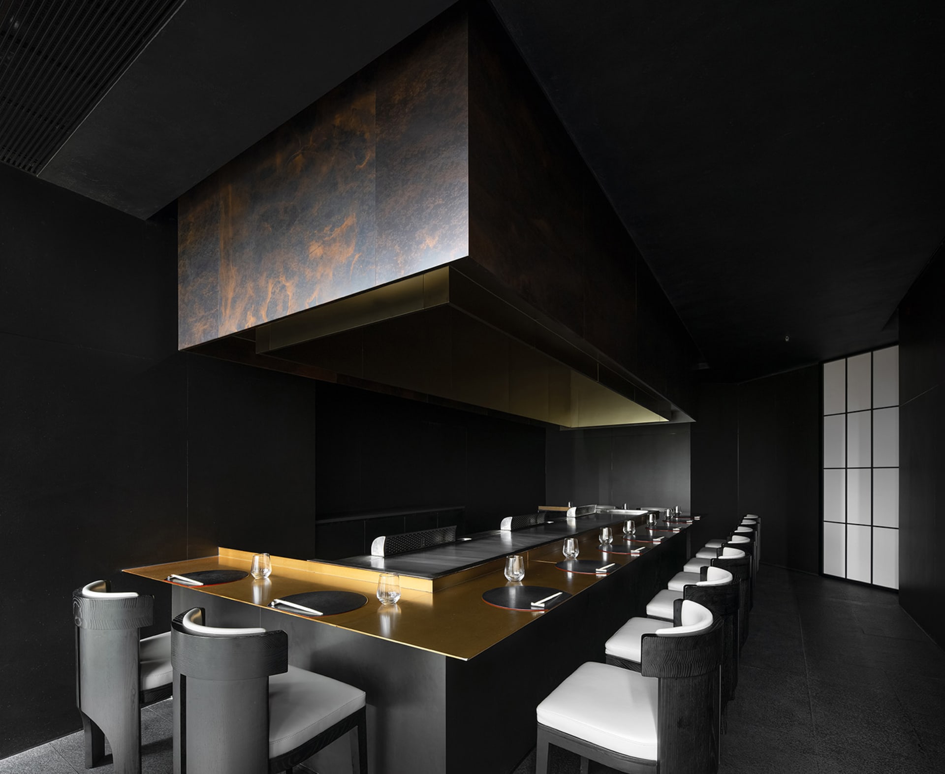 A sleek, modern restaurant interior featuring a black metallic bar counter and seating area.
