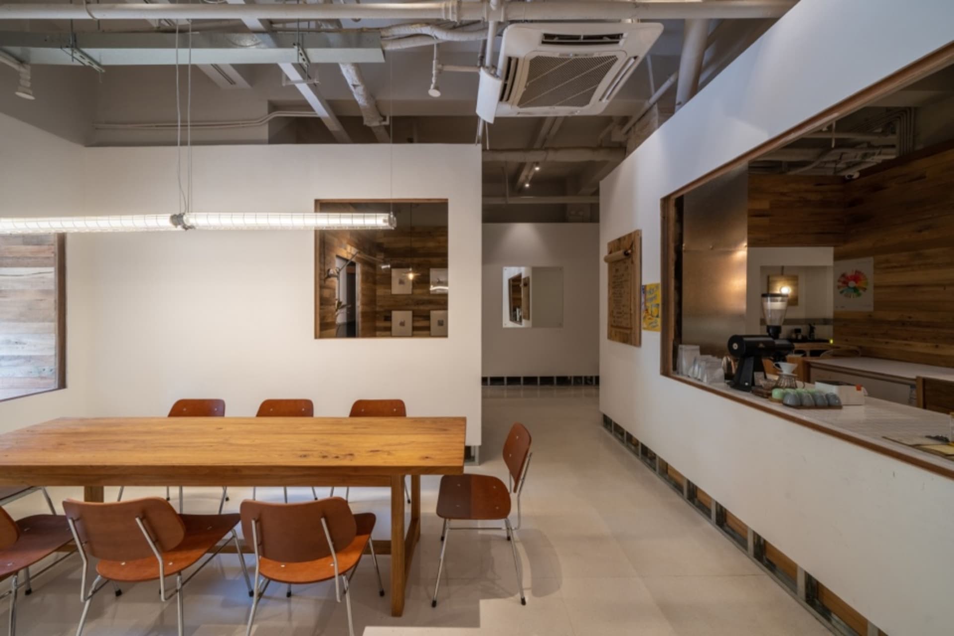 A minimalist coffee shop with a wooden interior, featuring tables and chairs, and a counter with a coffee machine.
